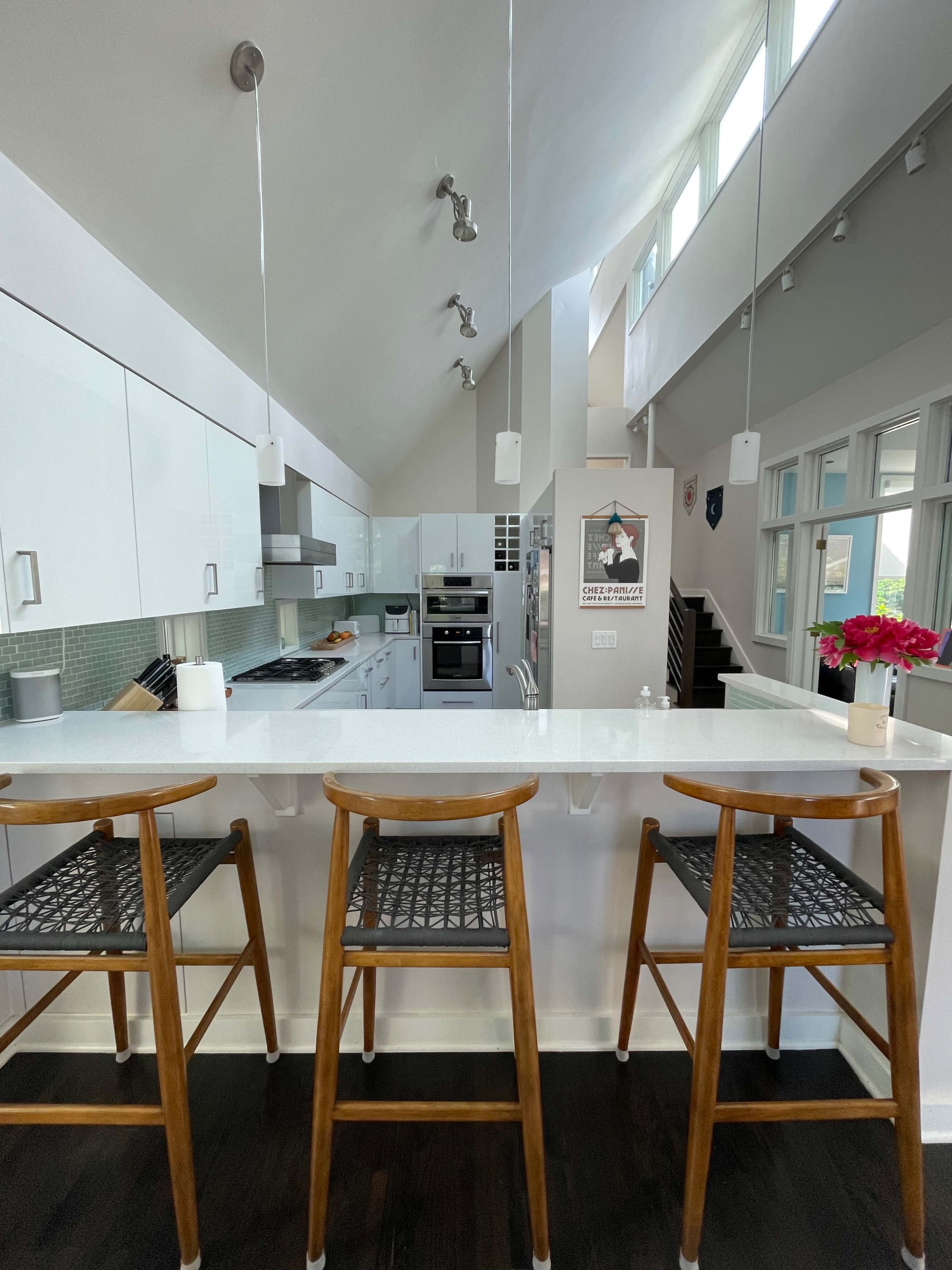 A modern kitchen with white cabinetry, stainless steel appliances, and three wooden bar stools arranged at a counter.