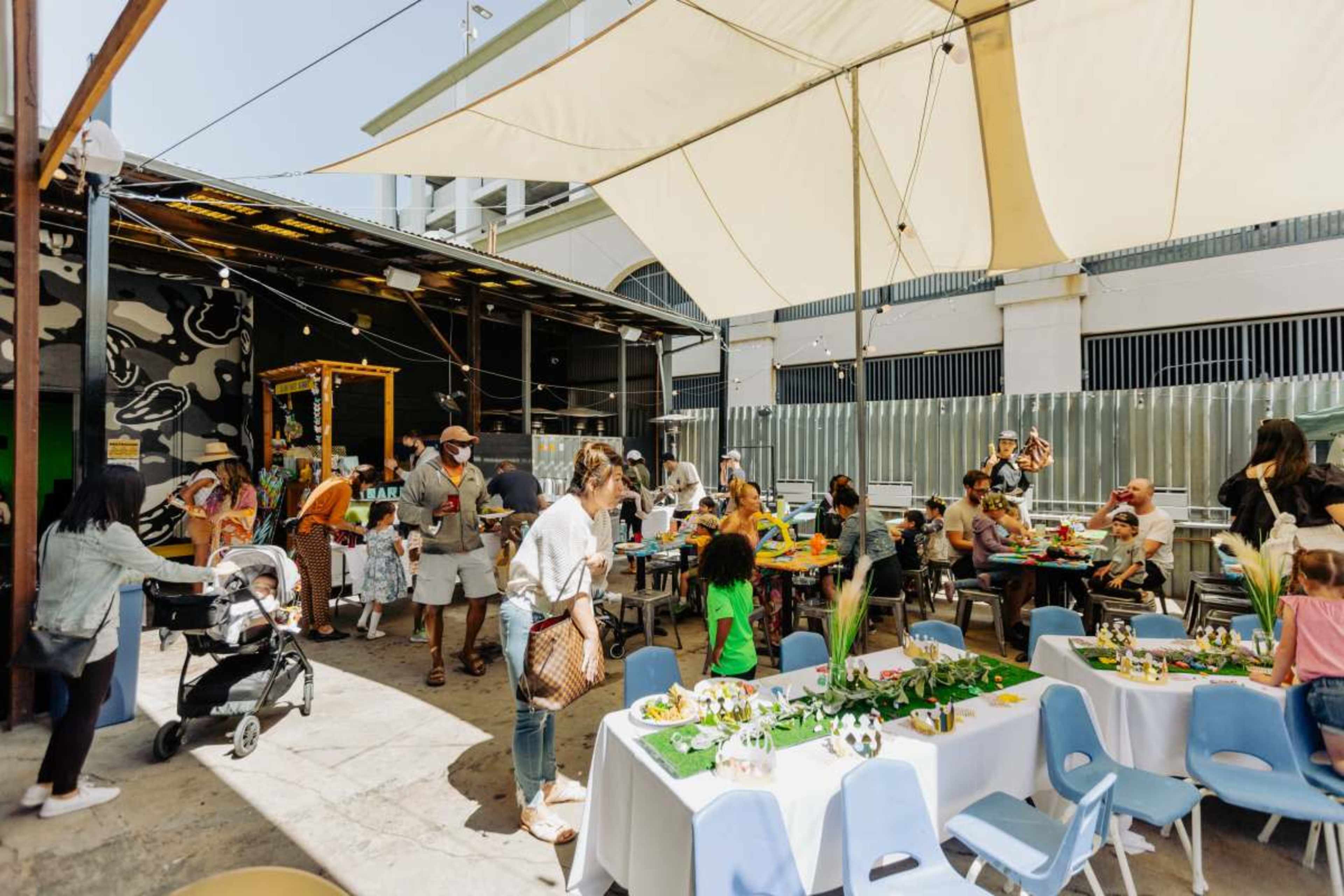 A crowd of people enjoys a lively outdoor gathering under a large canopy, with tables decorated for a celebration.