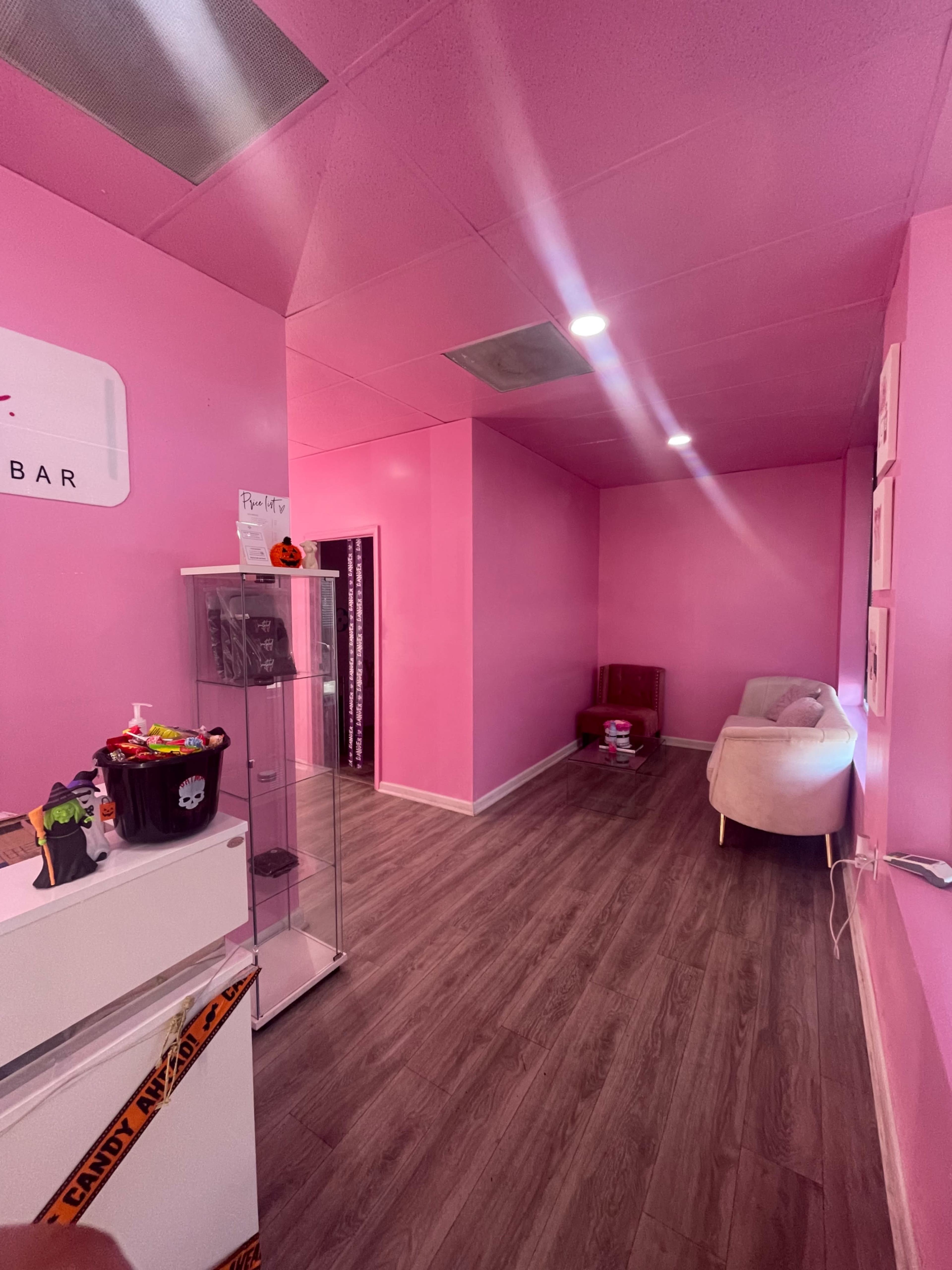 A room with pink walls, wooden flooring, a small seating area, and a display case on the left side.