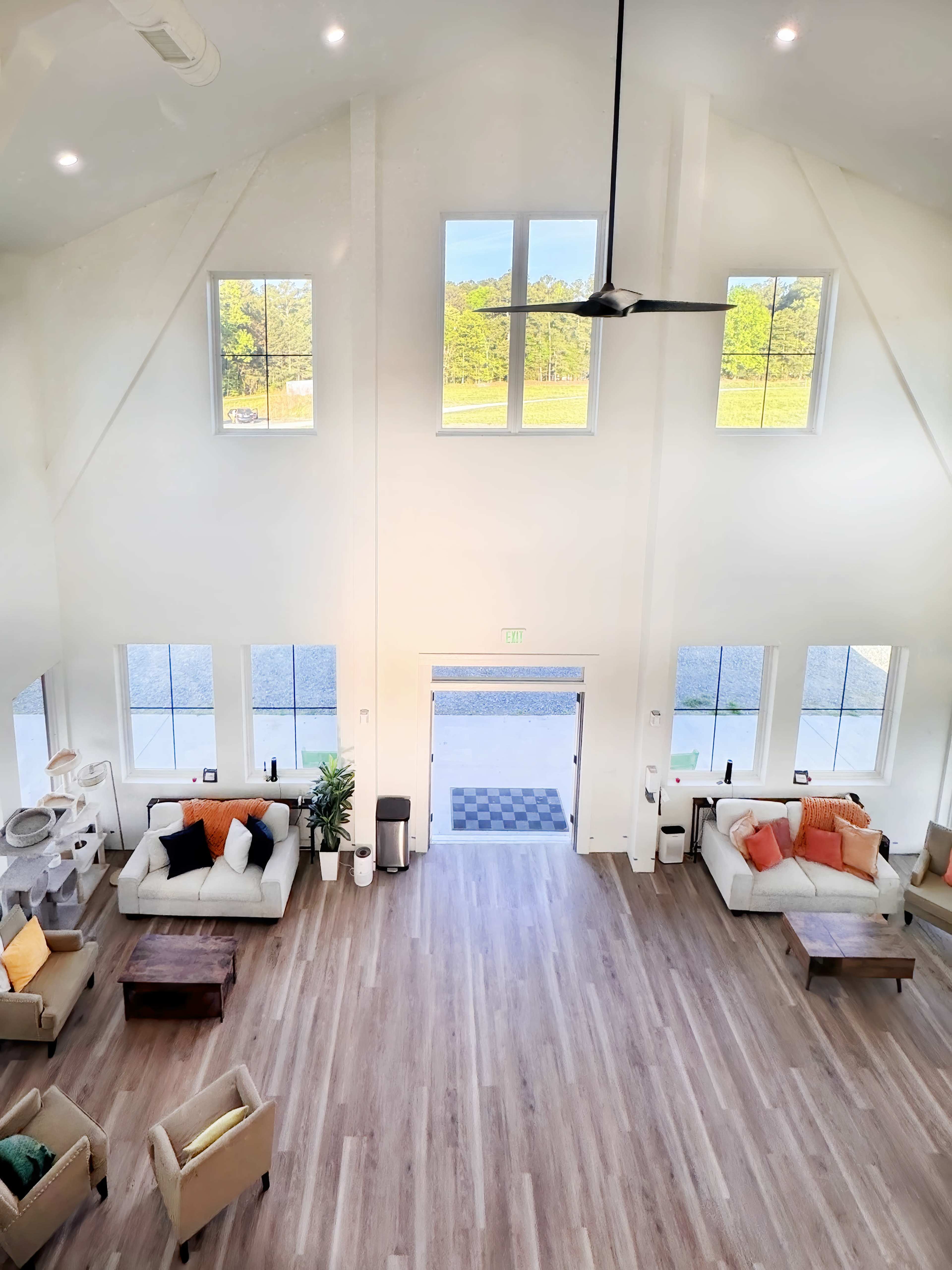 The image shows a spacious interior with high ceilings, large windows, and a modern seating area furnished with sofas and a table.