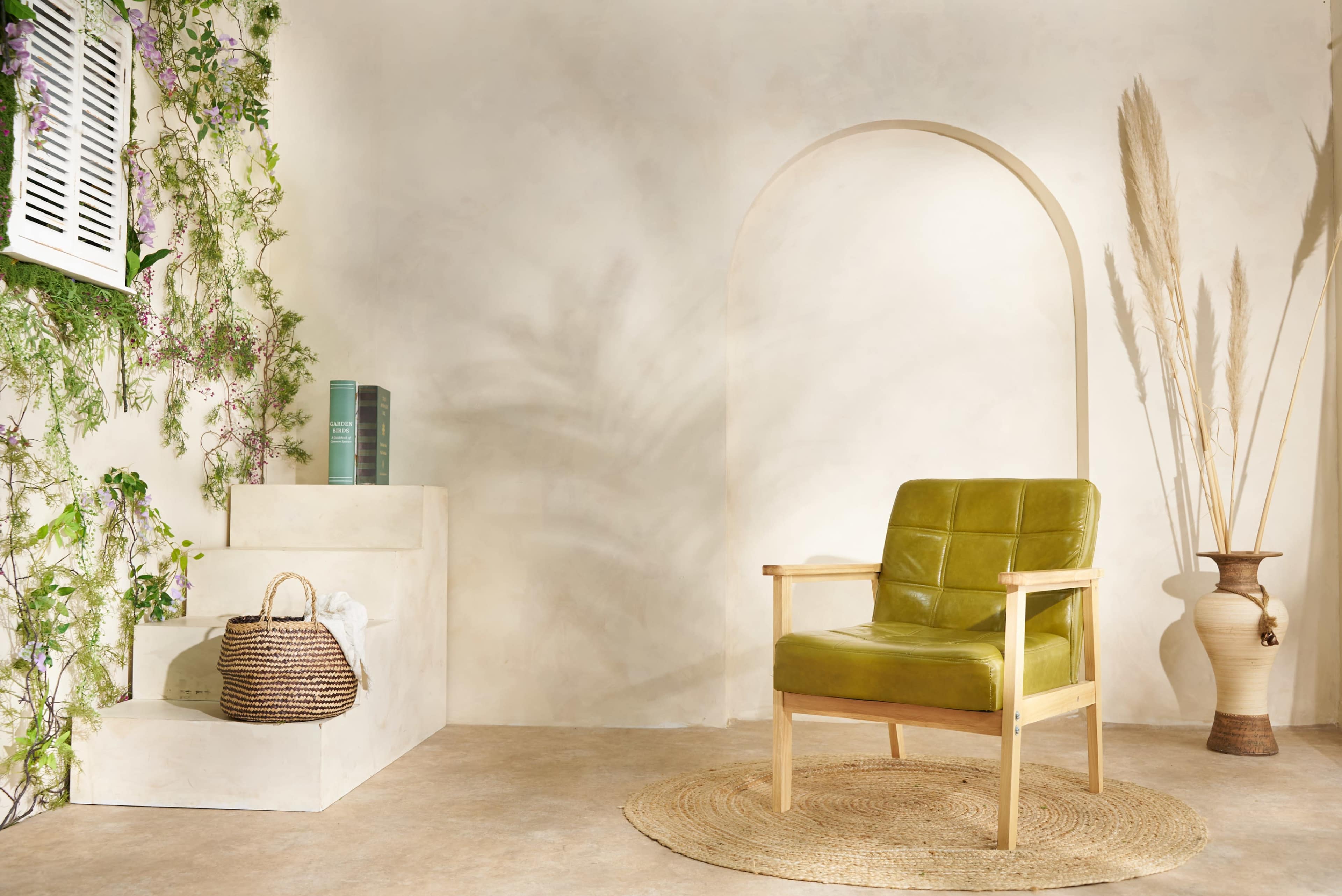 A green leather chair is positioned beside decorative steps and a tall vase, against a softly painted wall adorned with plants.