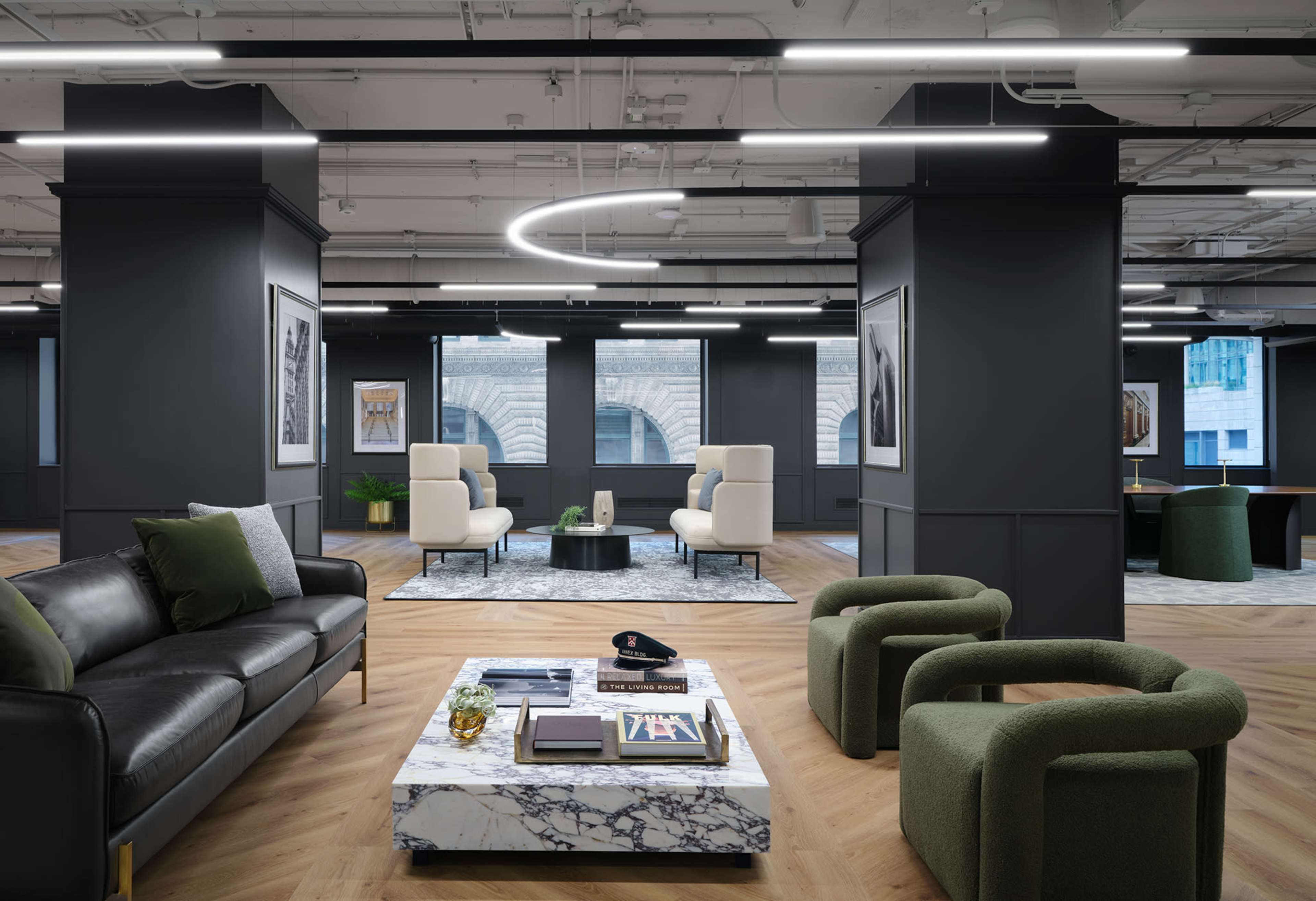 The image shows a modern office interior with a black leather sofa, marble coffee table, and several seating areas, illuminated by circular LED light fixtures.