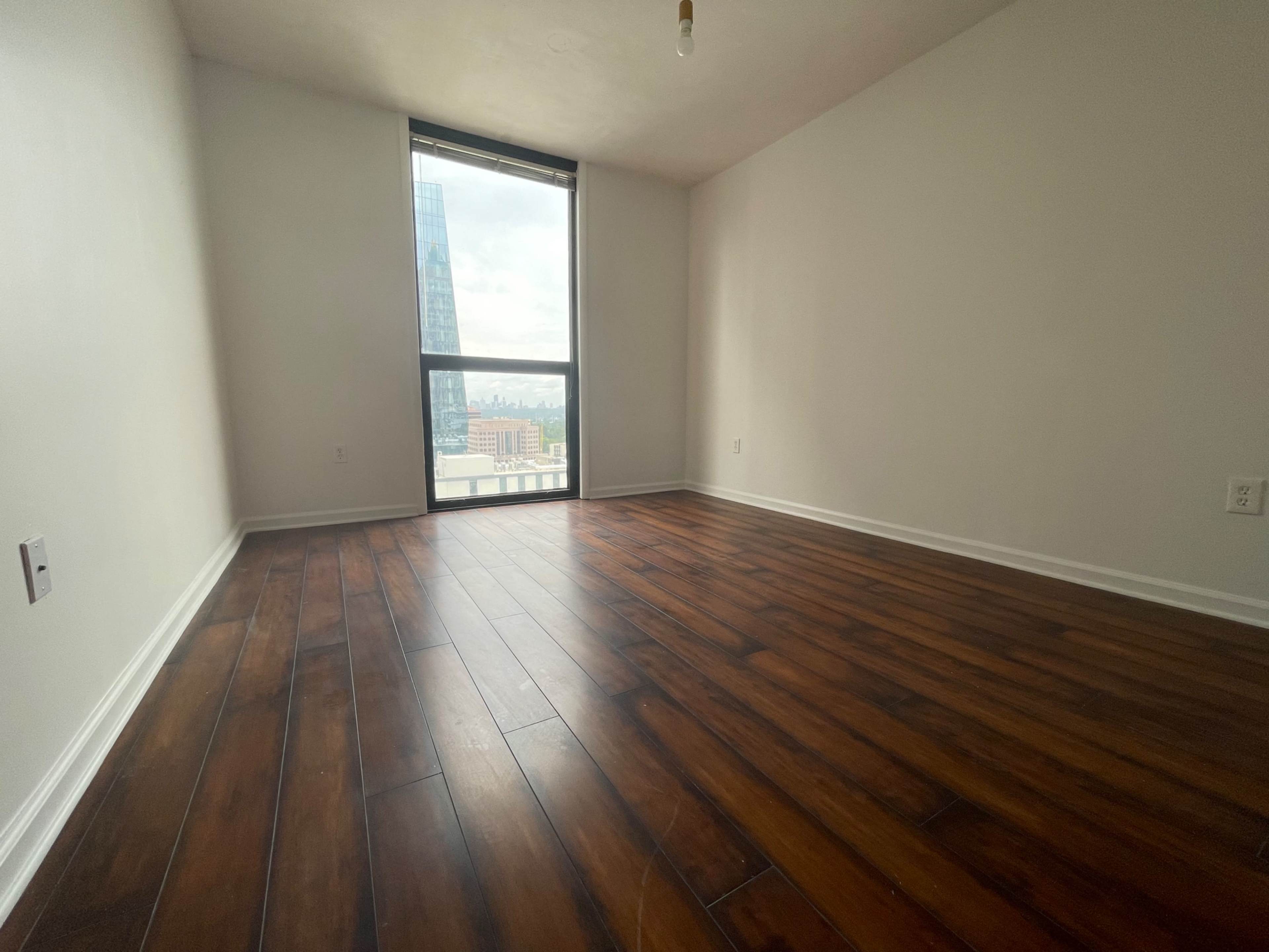 An empty room with hardwood flooring and a large window overlooking a cityscape.