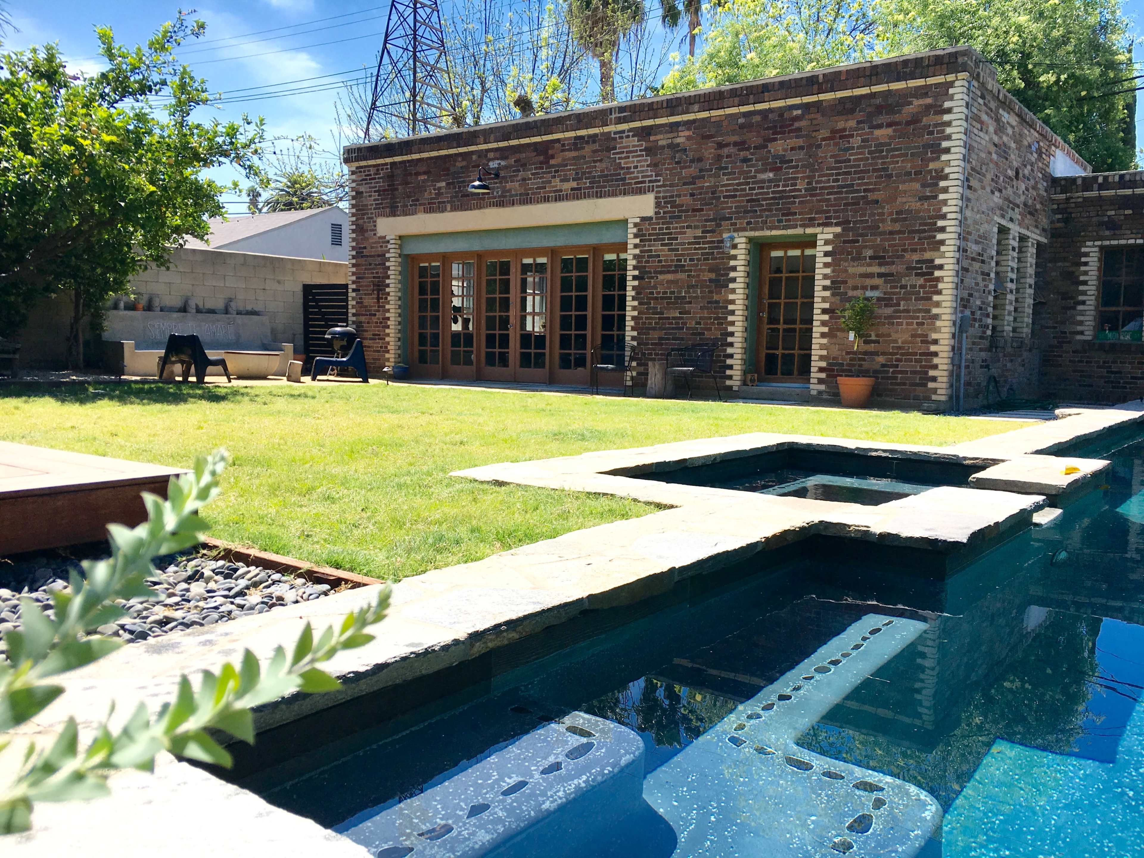 A modern brick house adjacent to a swimming pool with a stone edge and a grassy yard.