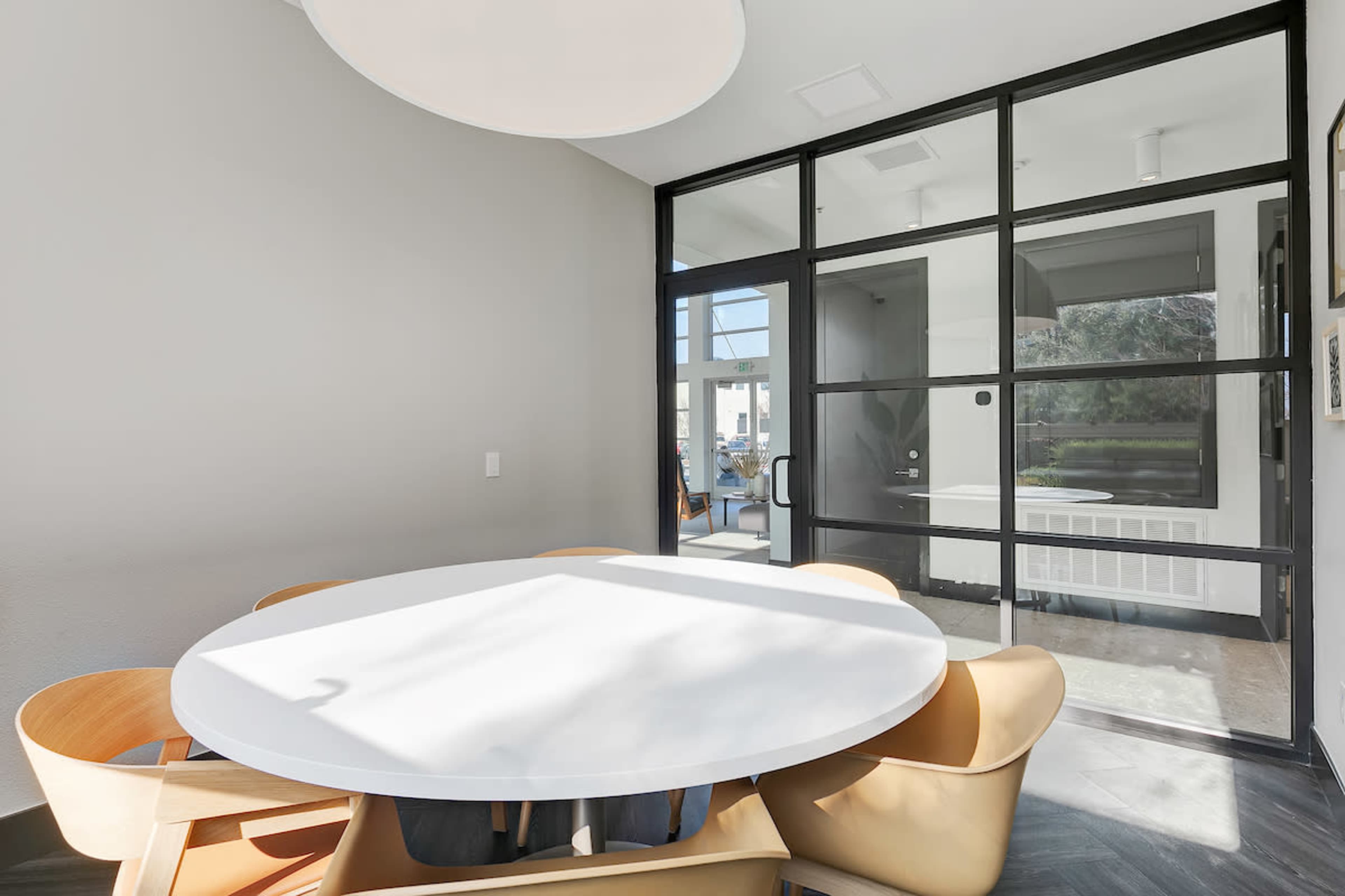 A round dining table surrounded by wooden chairs is set in a room with large glass windows and minimalist decor.