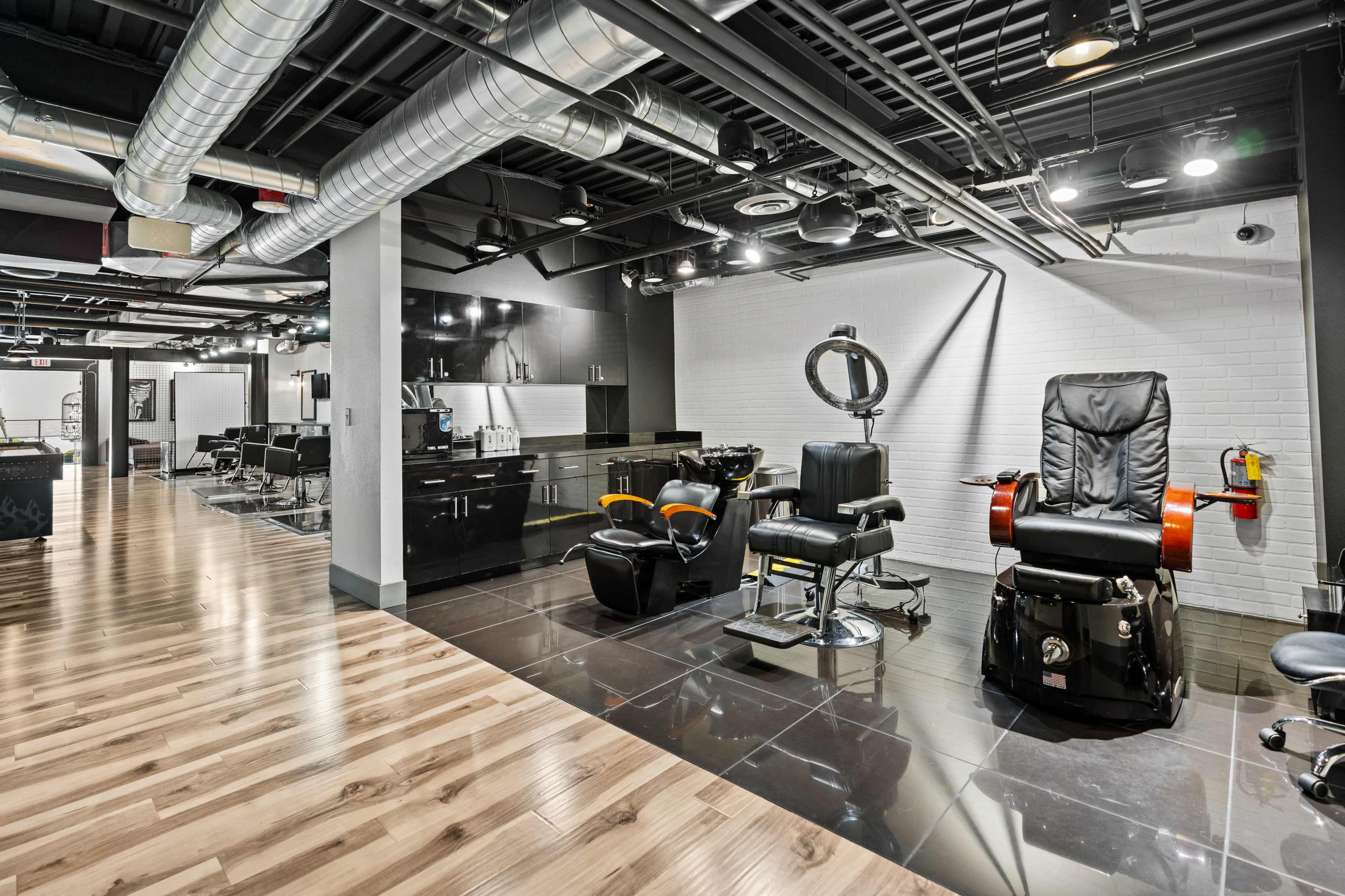 The image shows a modern barber shop setup with sleek black styling stations and wooden flooring.