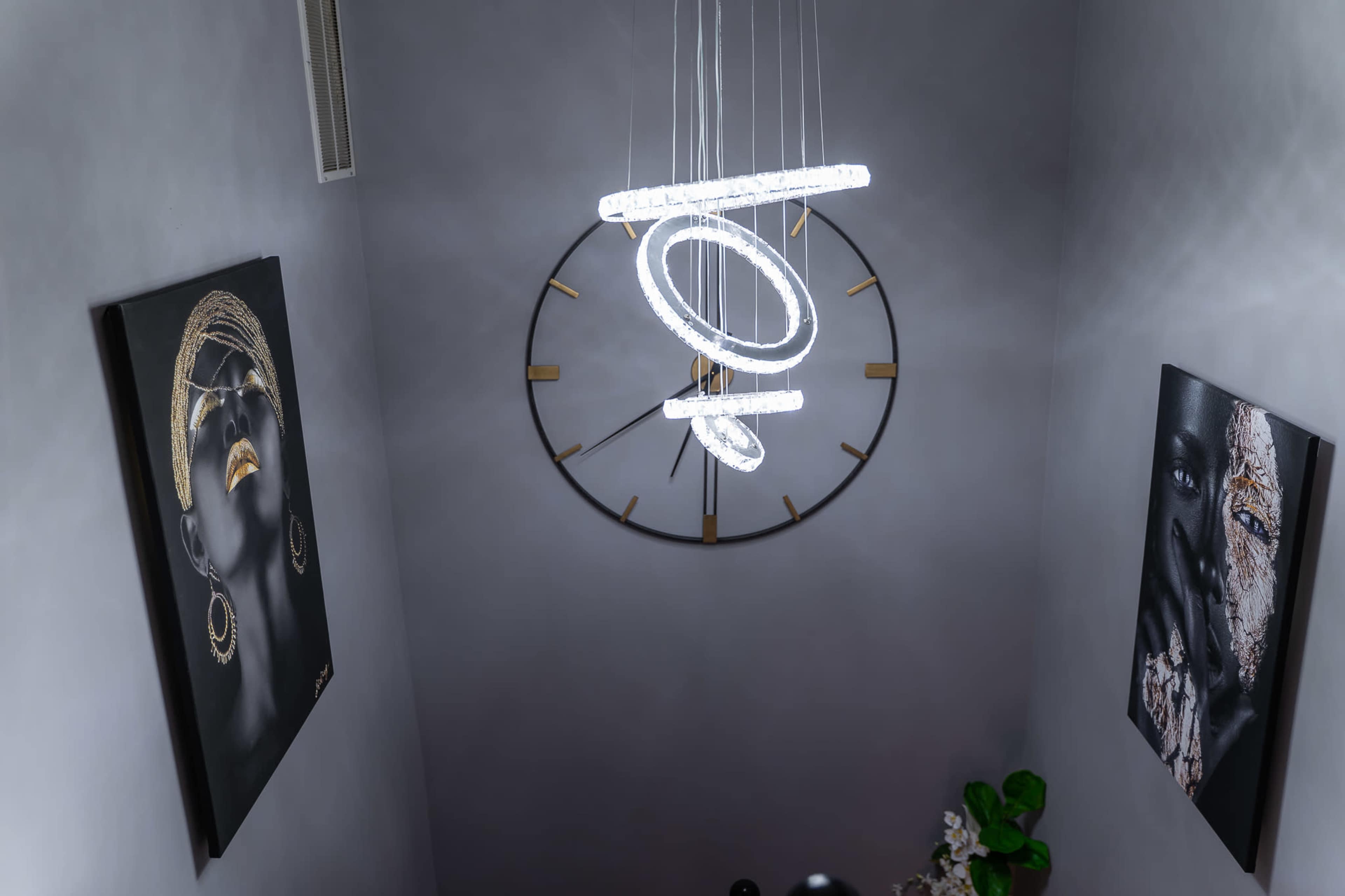 A modern staircase features a circular light fixture and a large wall clock, flanked by two black-and-white portraits adorned with gold accents.
