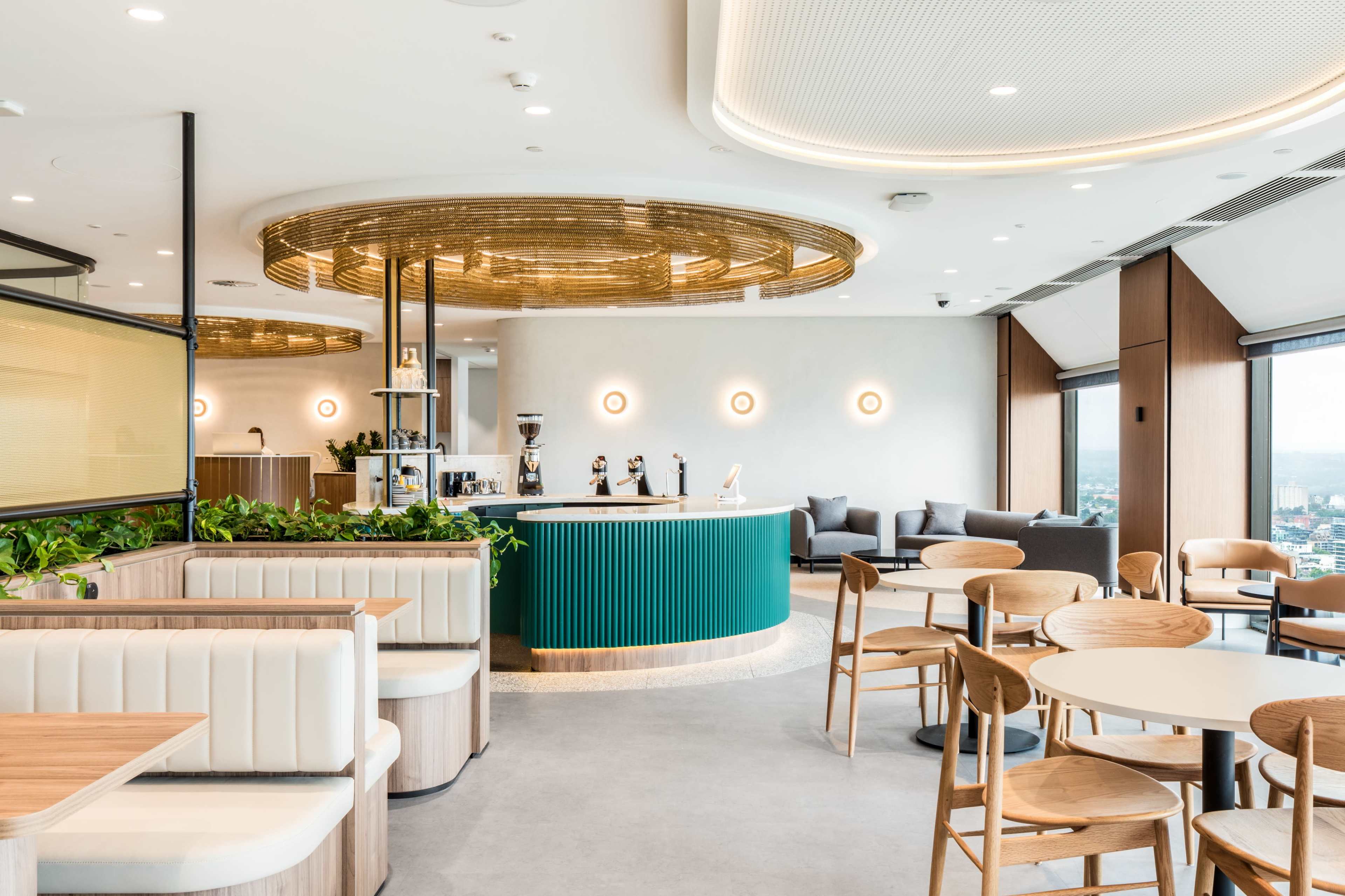 A modern café interior features a circular bar with a green backsplash, surrounded by seating areas and large windows.