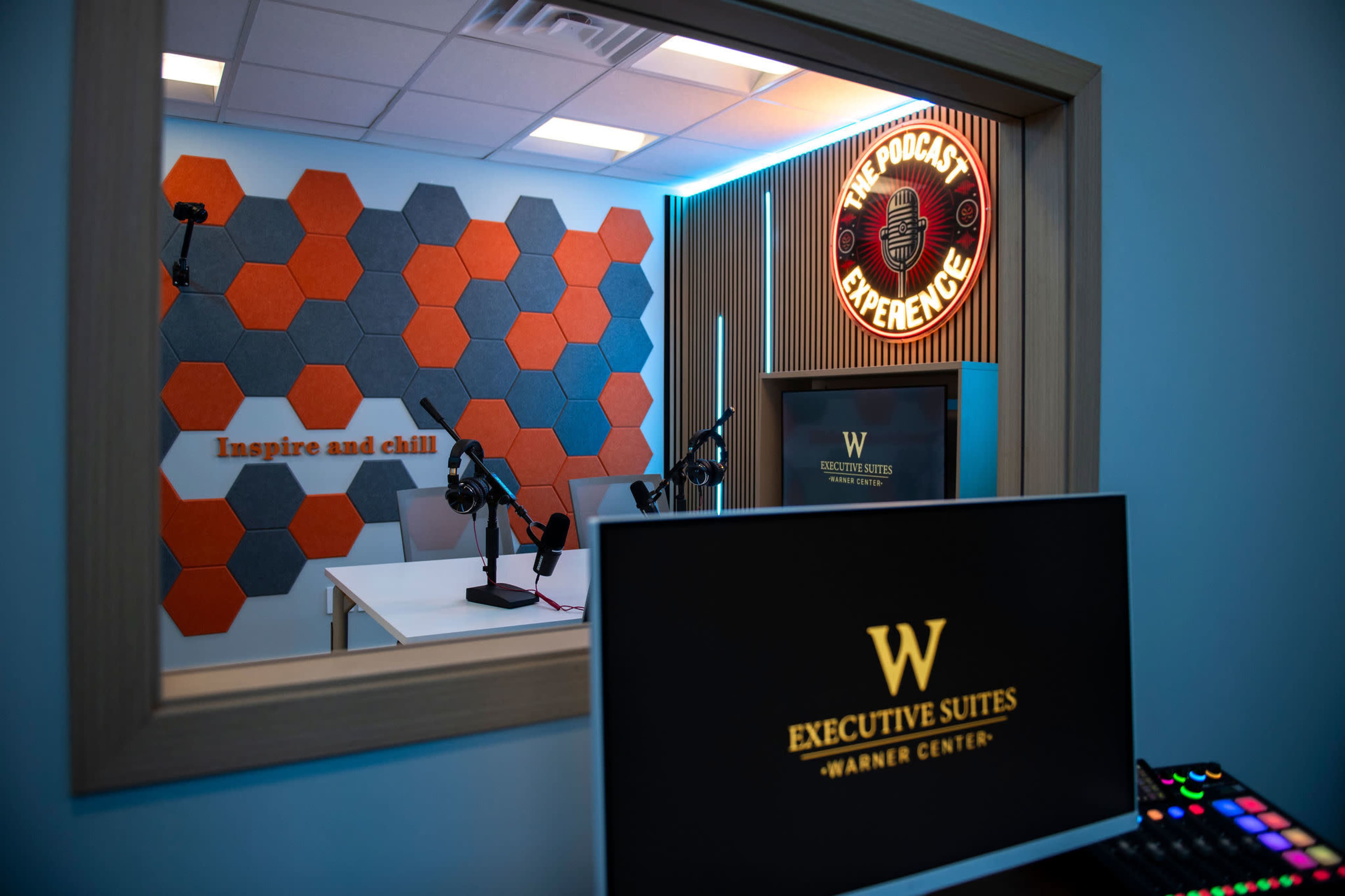 The image shows a modern podcast studio with hexagonal wall panels and microphones set up on a table, featuring a sign that reads "Inspire and chill."