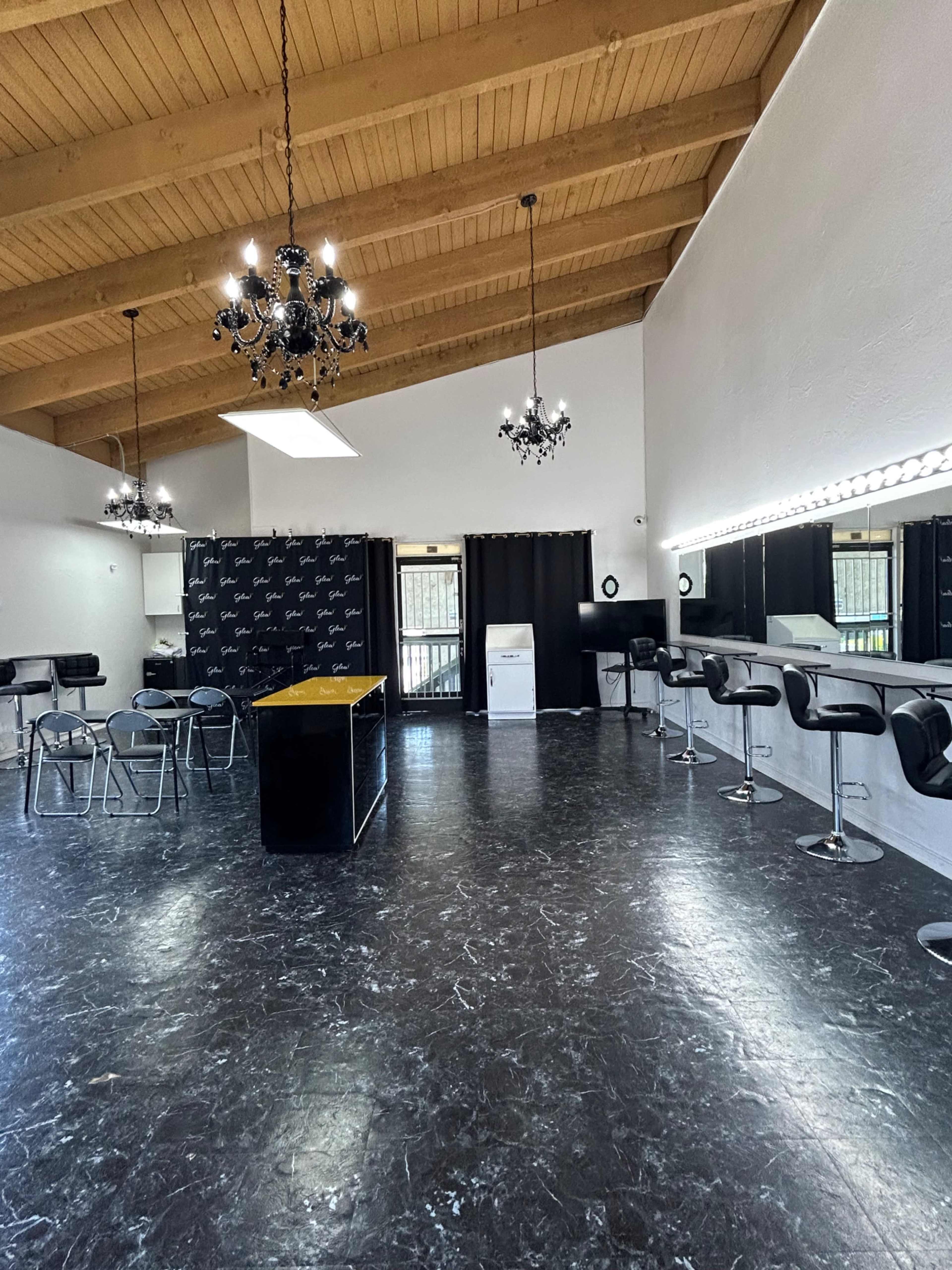 A spacious salon interior with high wooden beams, a black and white color scheme, a central island, bar stools, and mirrors along one wall.