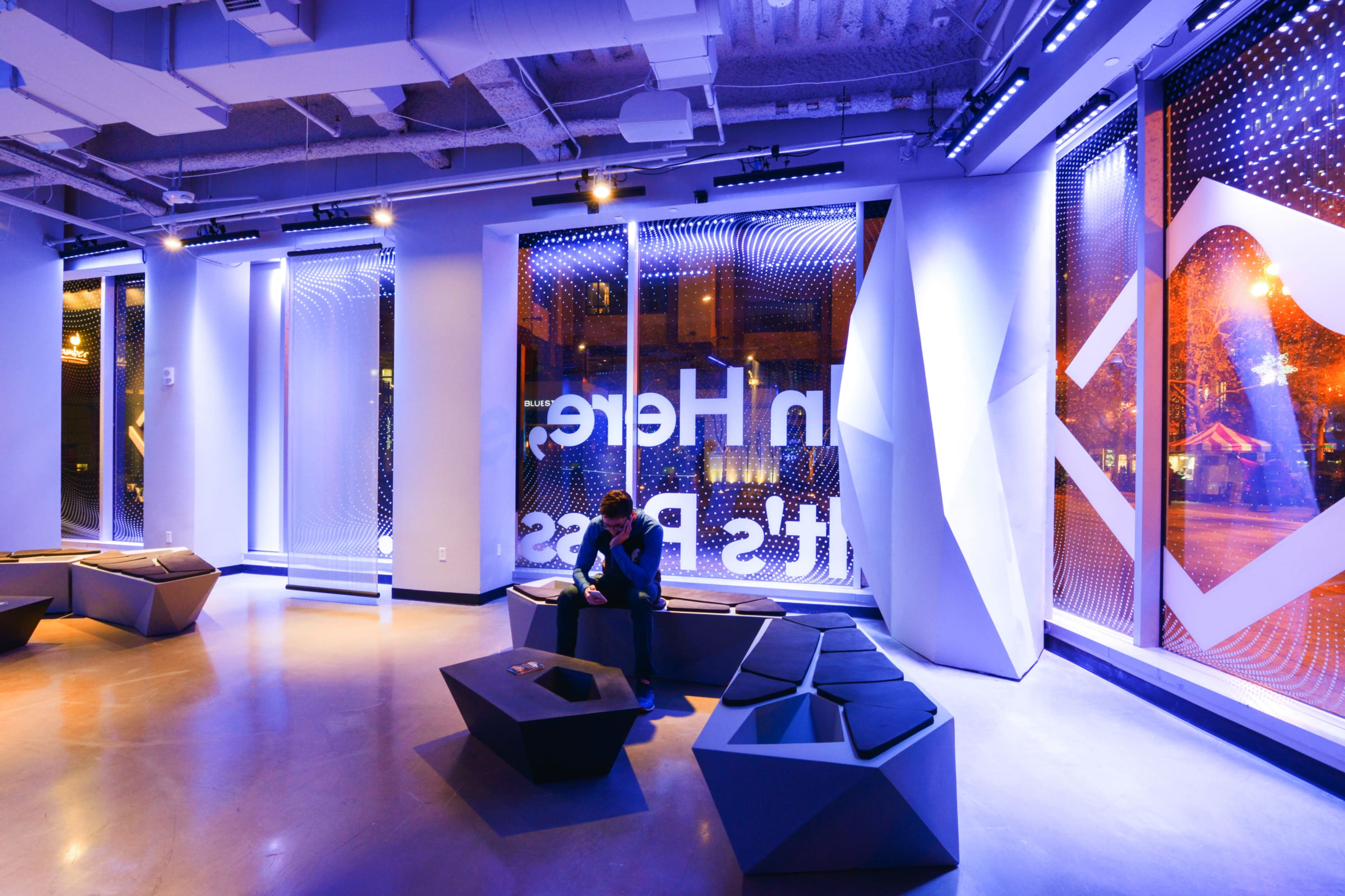 A modern interior space with geometric seating and large windows displaying a vibrant cityscape at night.