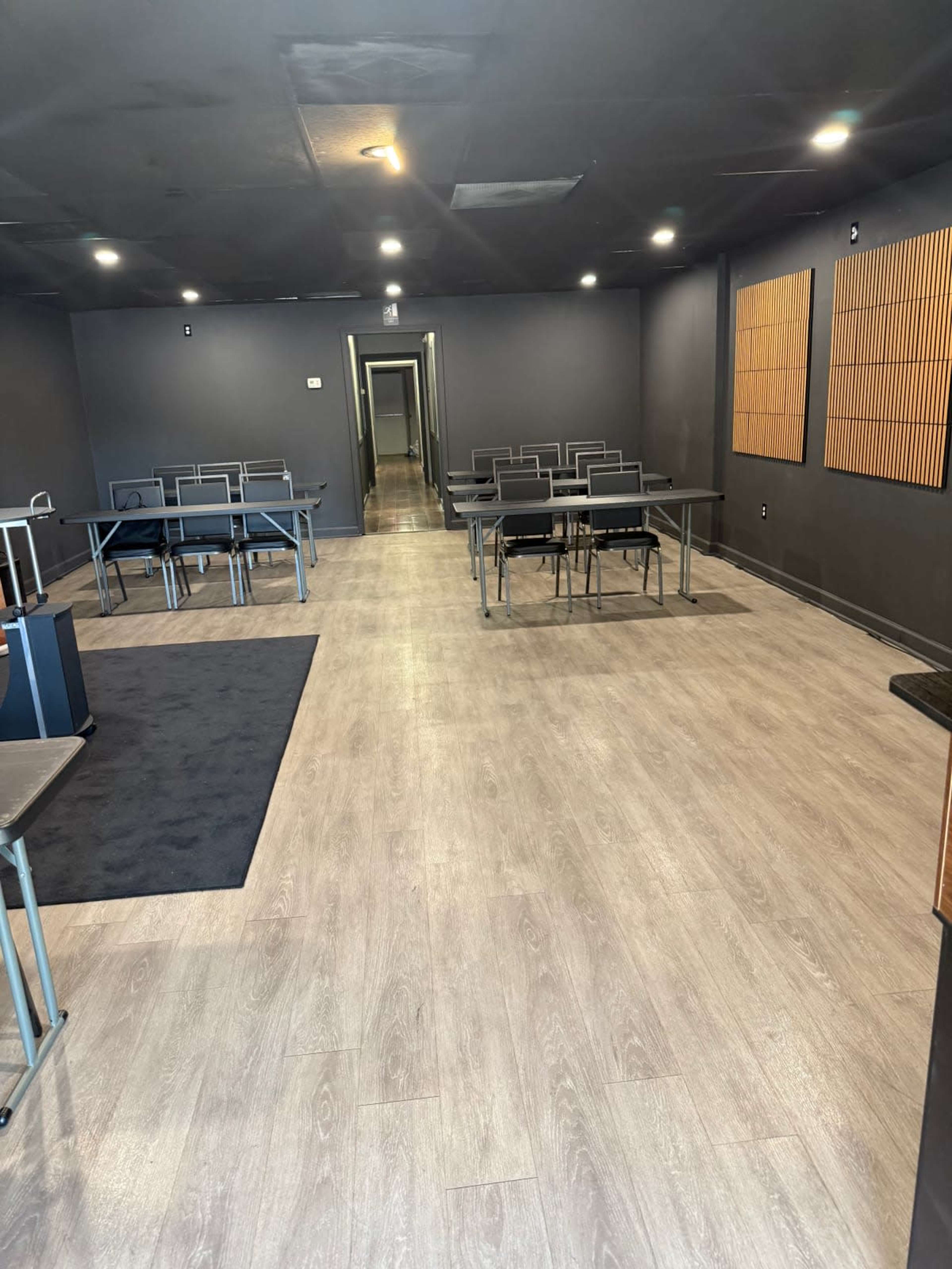 The image shows an empty room with a dark-colored interior featuring several tables and chairs arranged in rows.