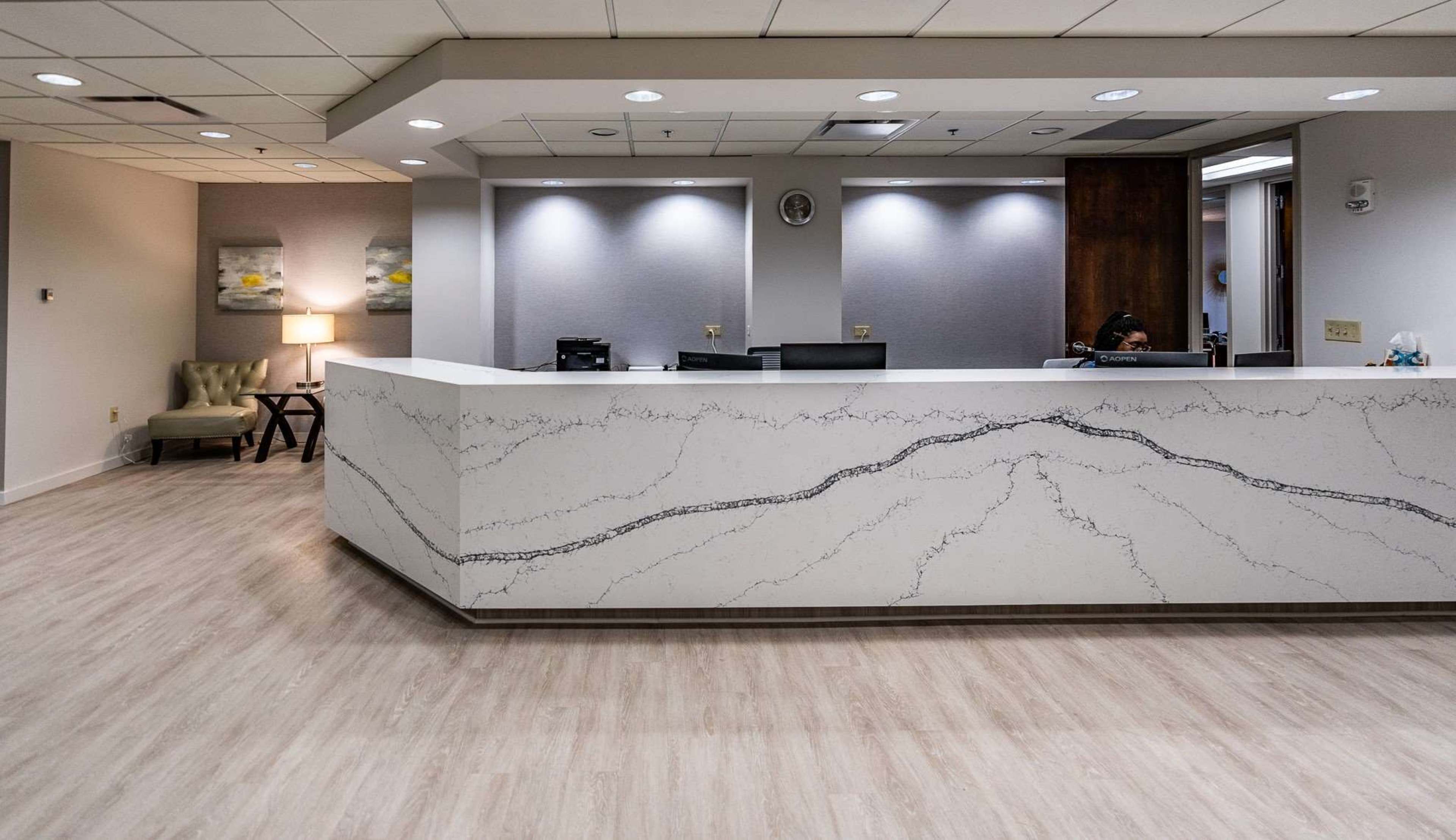 A reception area features a marble-patterned counter, beige flooring, and a soft seating area with a lamp.