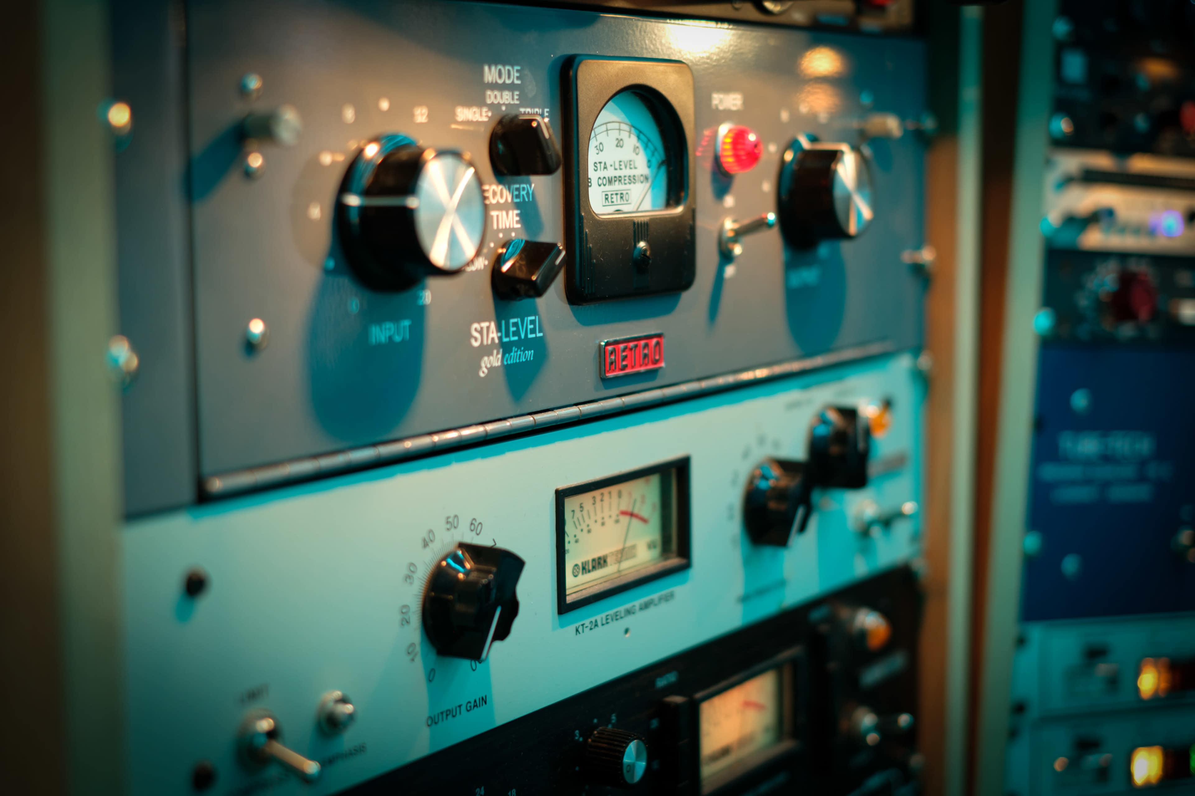 The image shows a close-up of audio equipment with various dials, knobs, and meters mounted in a rack.