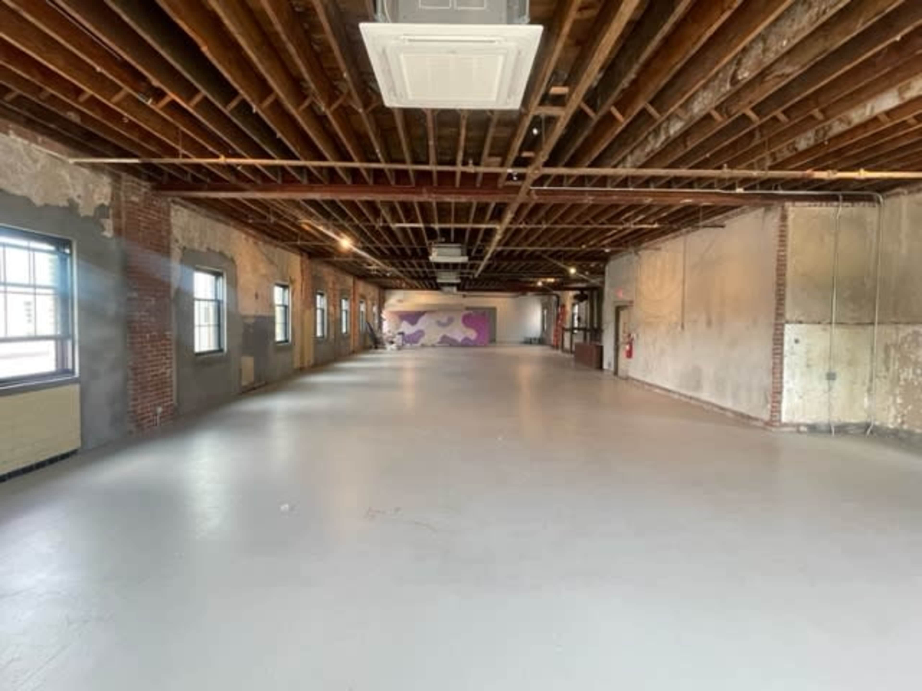 A spacious, empty room with exposed brick walls and wooden beams overhead.