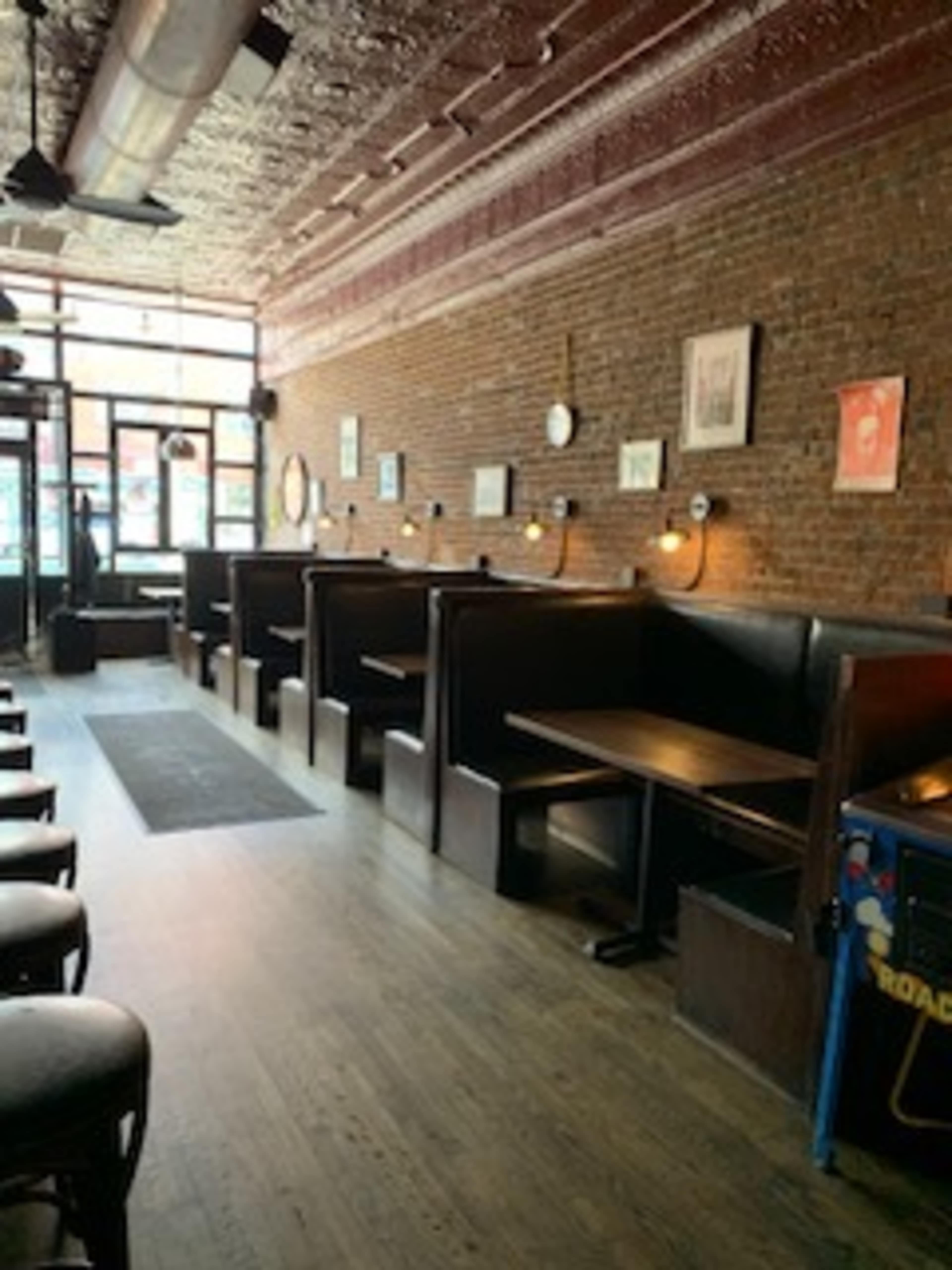 The image shows the interior of a café or restaurant featuring wooden booths along a brick wall, with a few framed pictures hanging above.