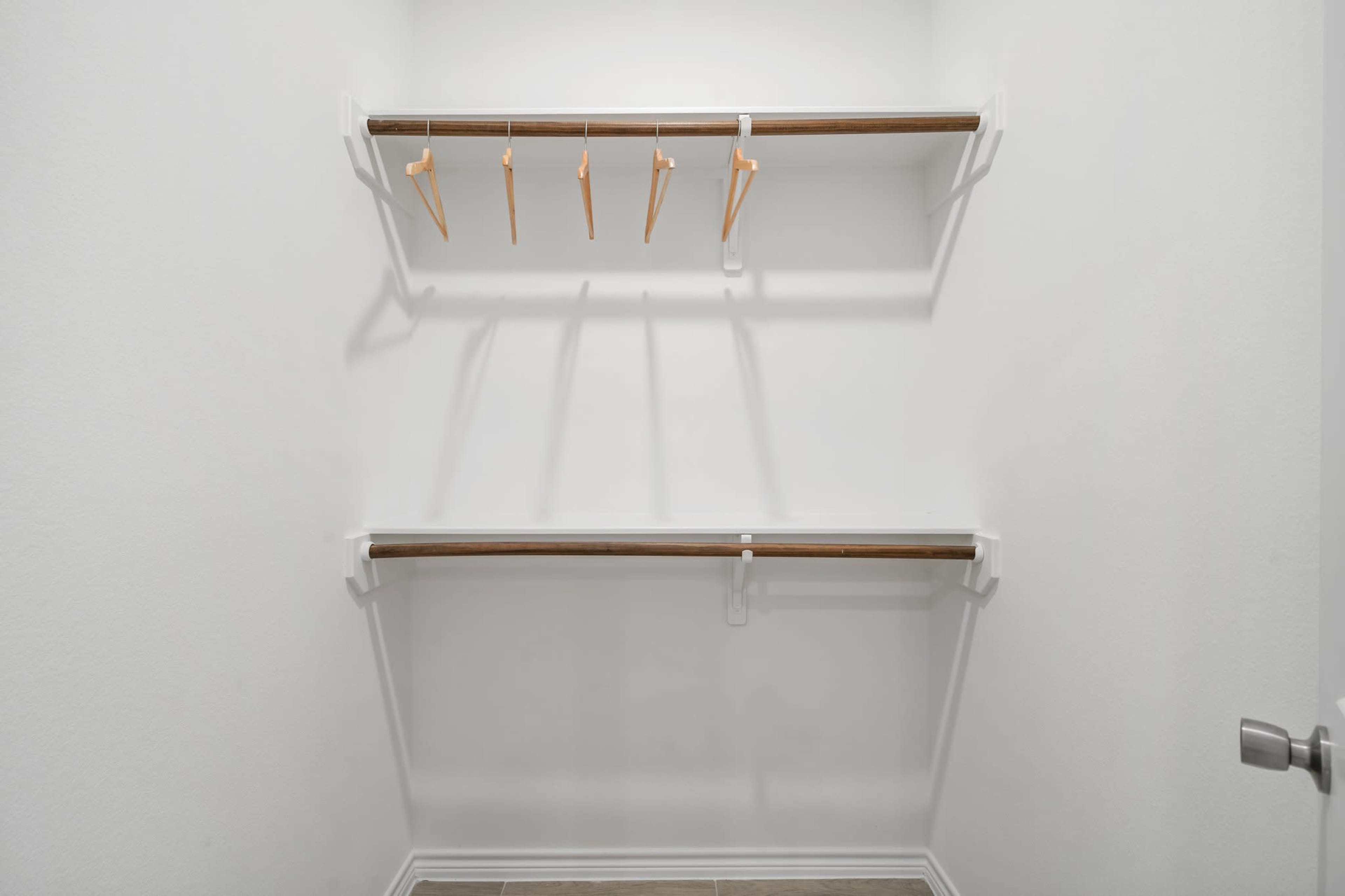 The image shows a minimalist closet with two wooden shelves and five wooden hangers attached to the top shelf.