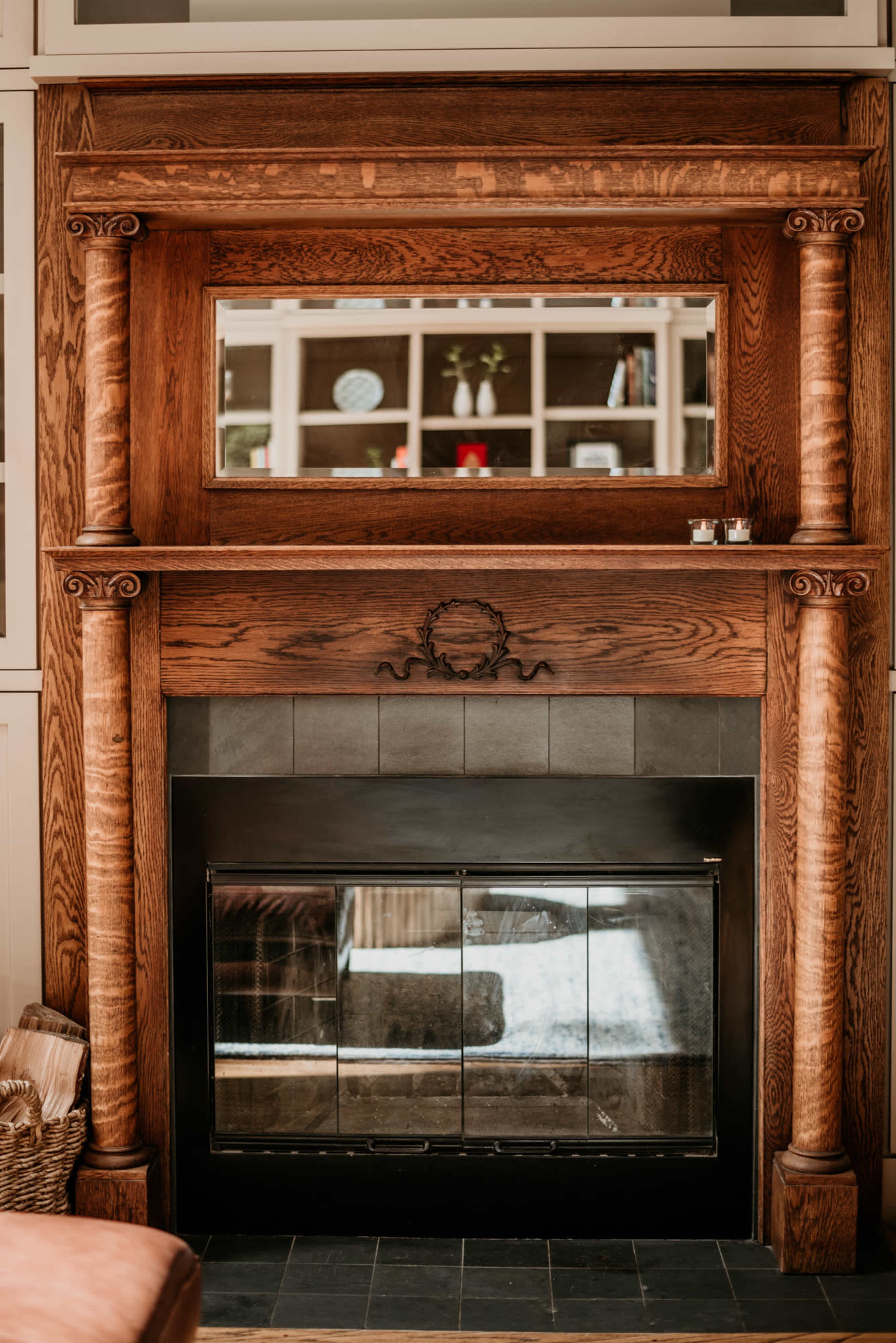 A wooden fireplace with a large mirror above it, framed by intricately carved columns.