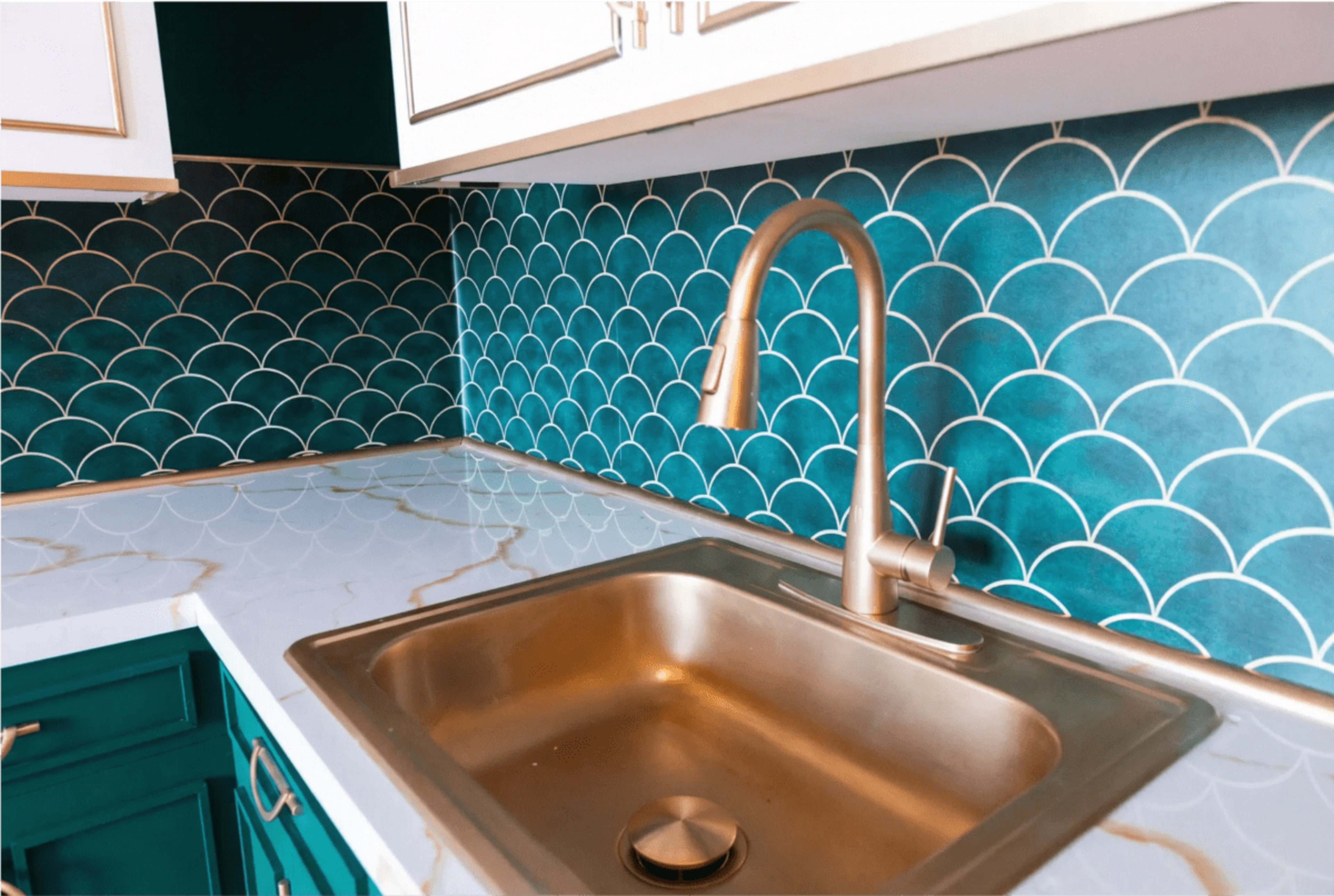 The image shows a kitchen sink with a metallic faucet set against a blue-green scalloped tile backsplash and a marble countertop.