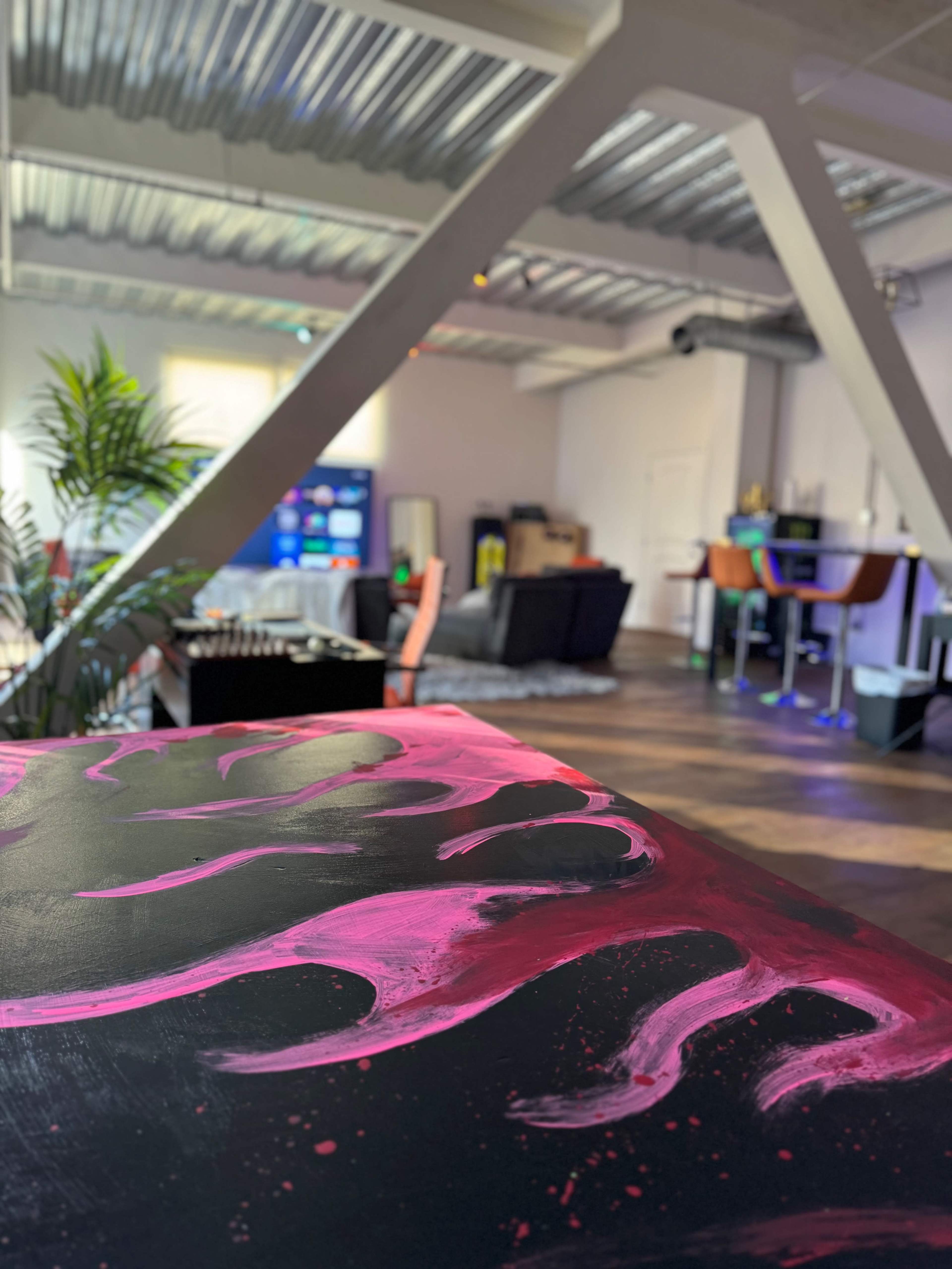 The image shows a creative workspace with a colorful, abstract painting in the foreground and various furniture and decor in the background.