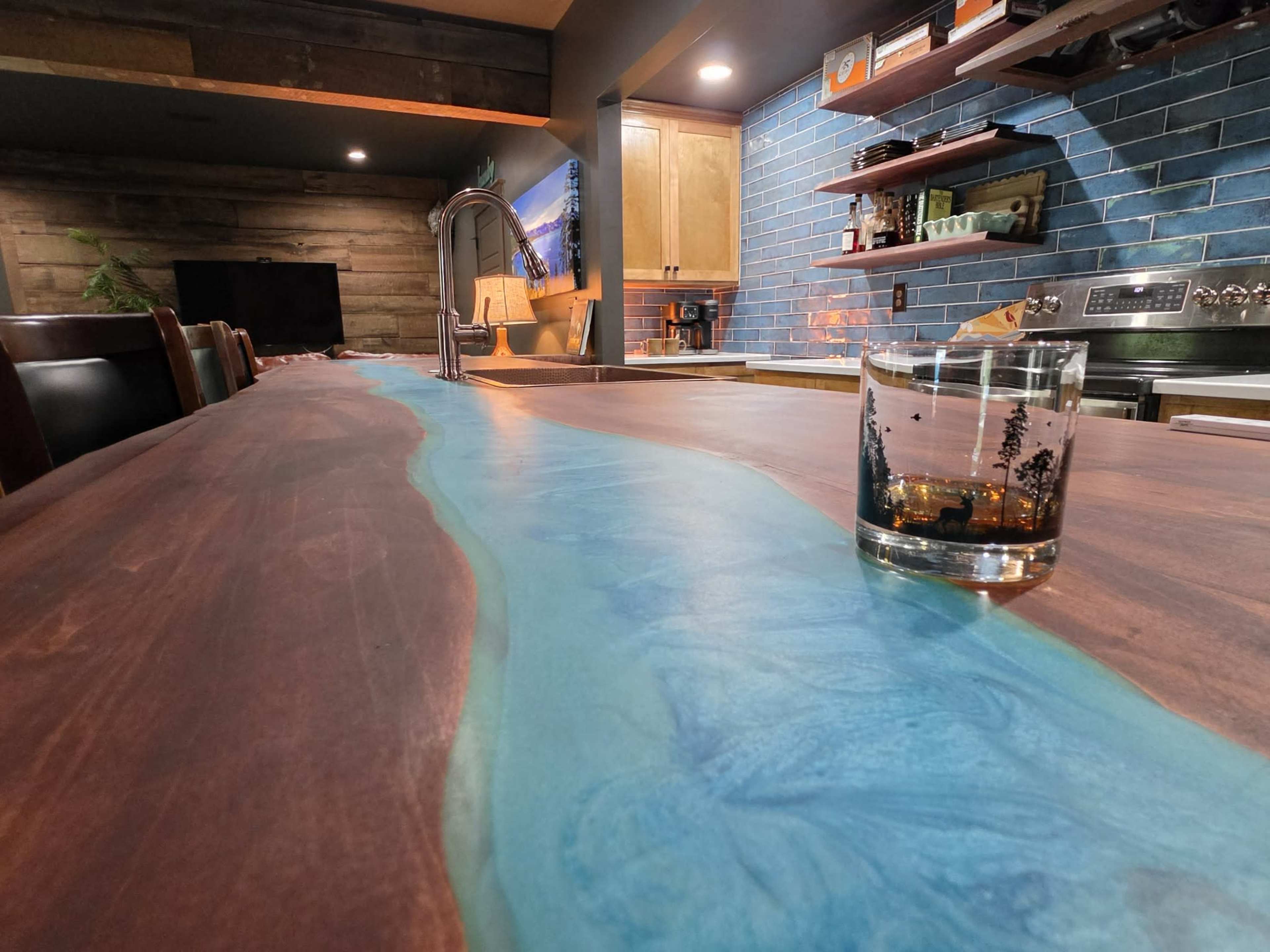 A wooden kitchen island features a flowing river-like blue epoxy design, with a glass resting on its surface.