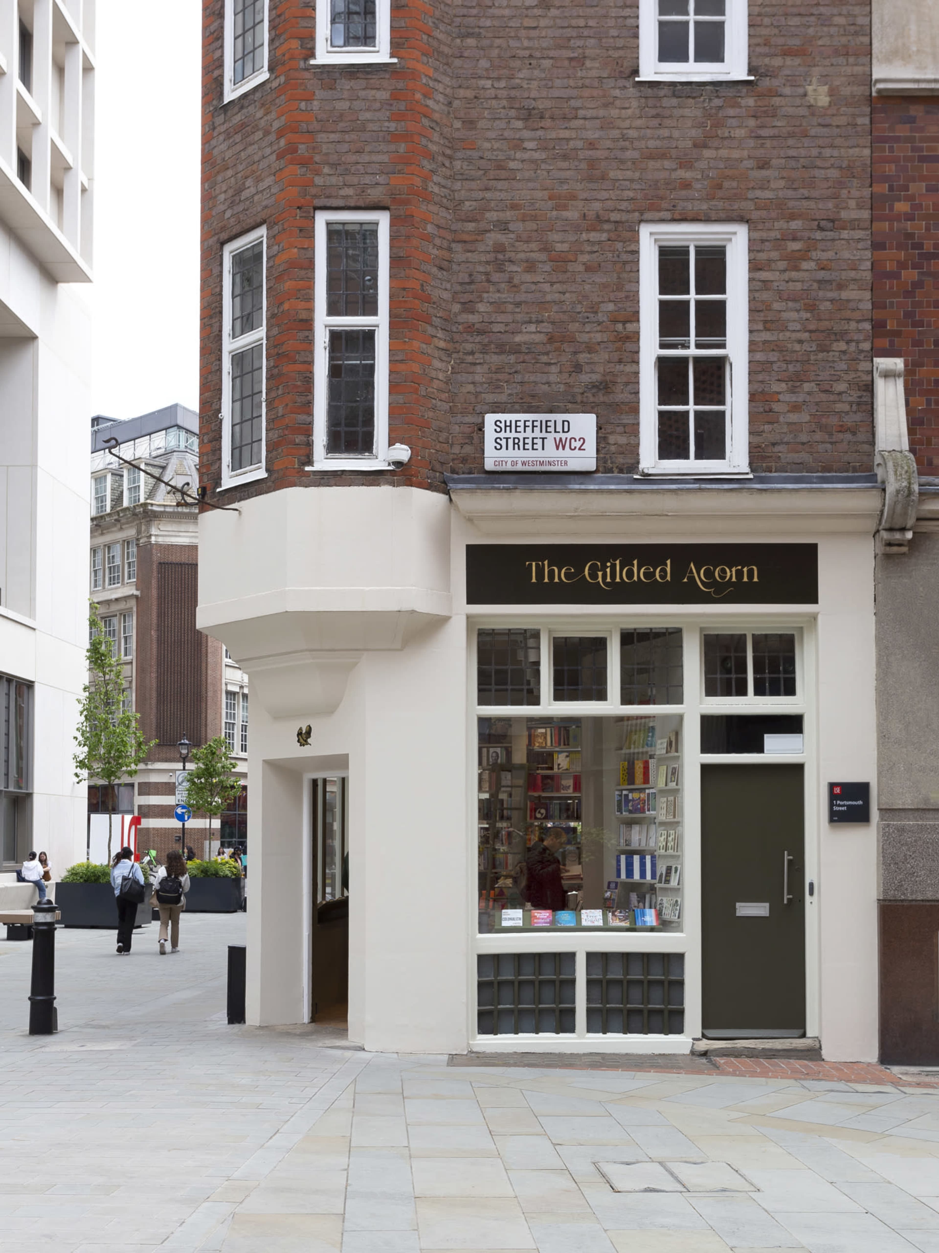 The exterior of a bookstore called "The Gilded Acorn," located at the corner of a brick building with a street sign for Sheffield Street.