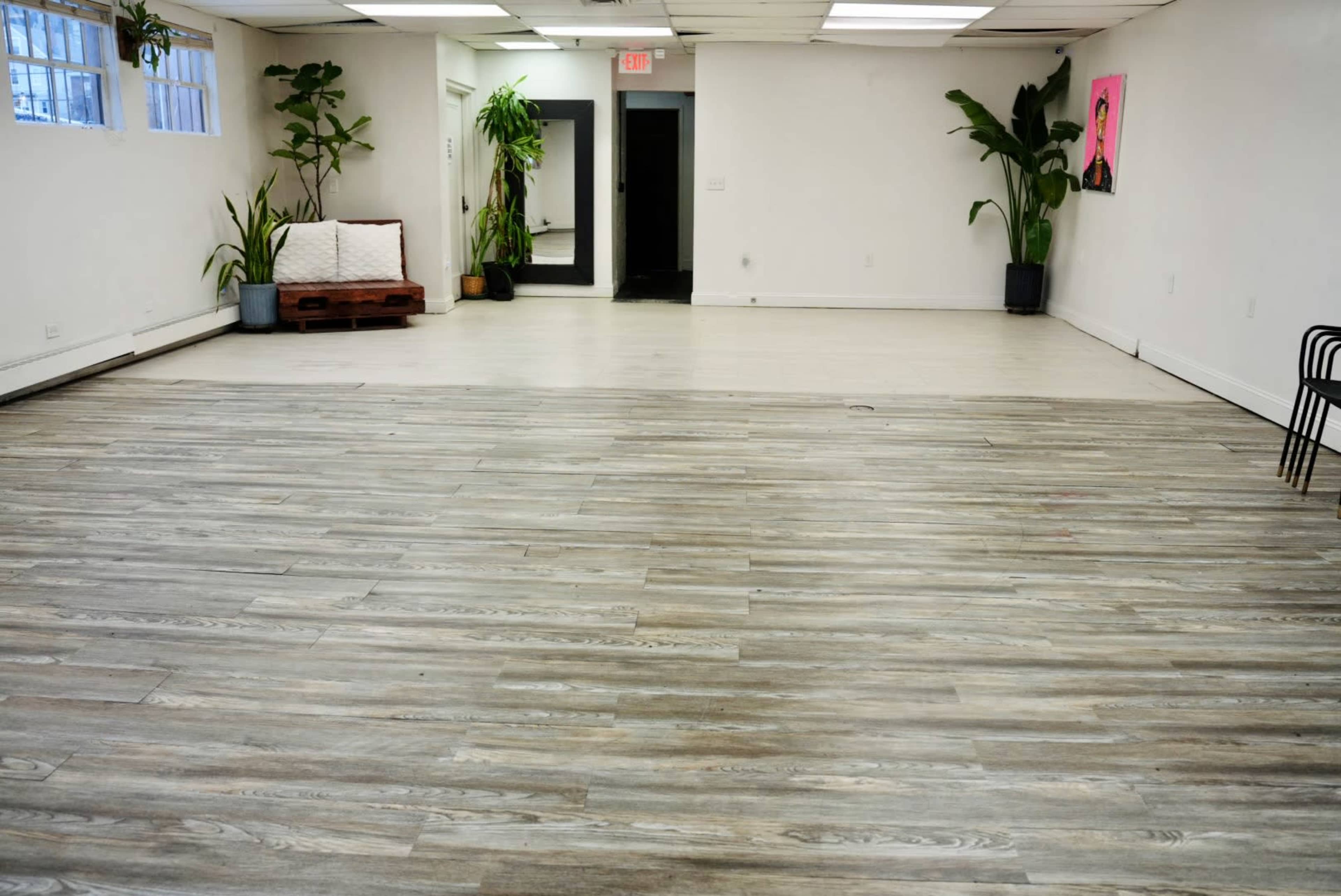 A spacious, empty room with wooden flooring, a white sofa against the wall, and several plants in pots.