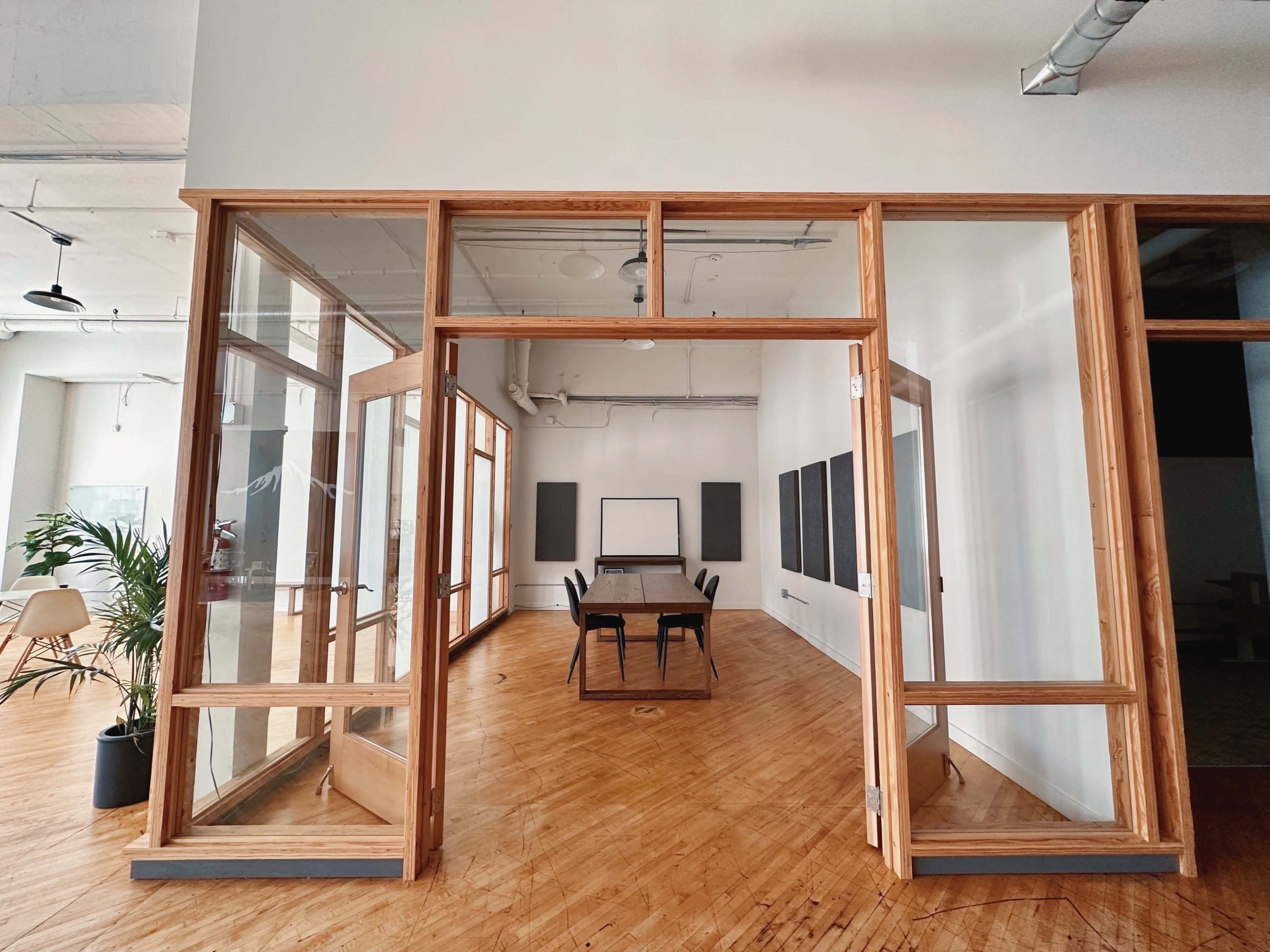 A modern office space with large glass-panel doors leading into a meeting room that features a long wooden table and black boards on the walls.