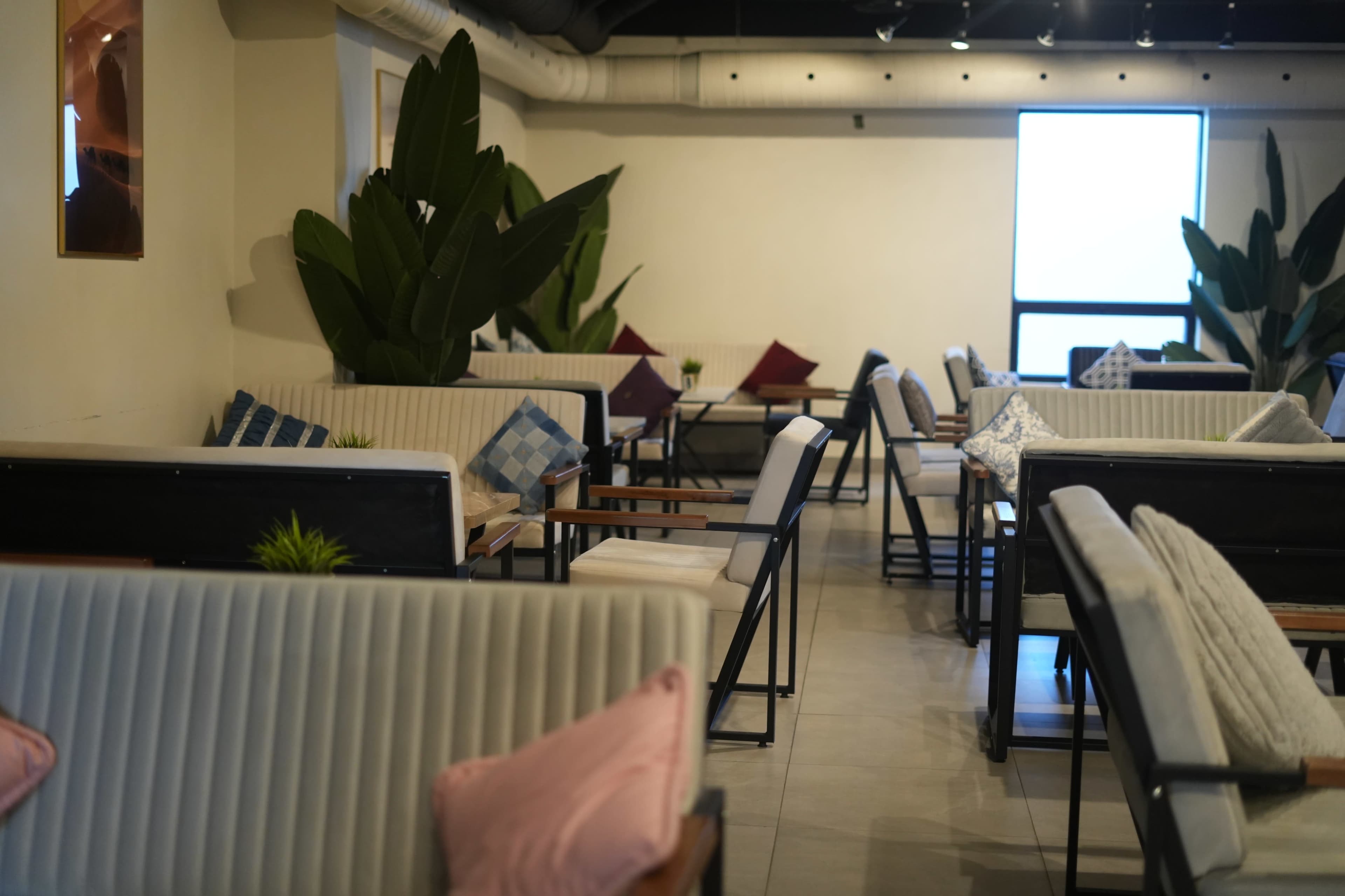 The image shows a modern café with rows of seating that include striped sofas, wooden tables, and decorative plants.