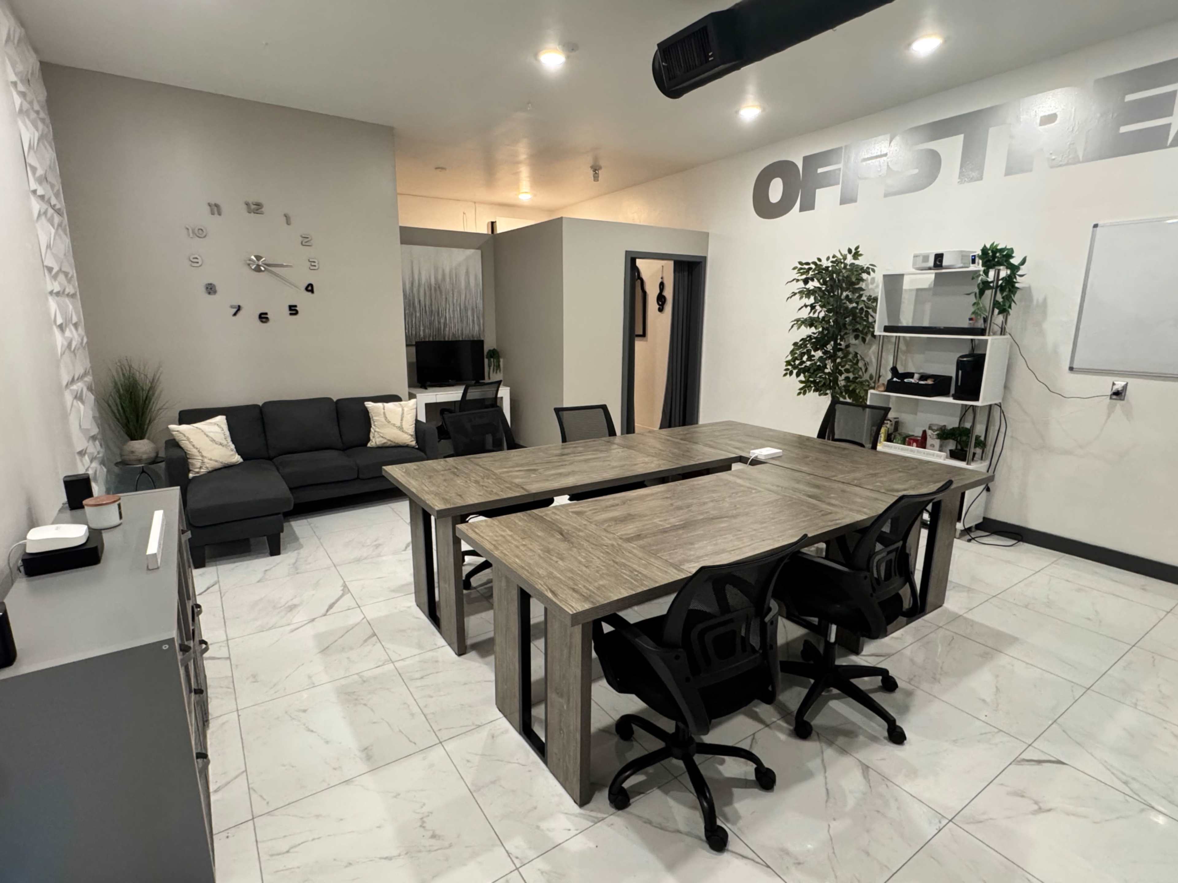 The image shows a modern meeting room with a large wooden table surrounded by black chairs, a gray couch in the corner, and minimalist decor on the walls.