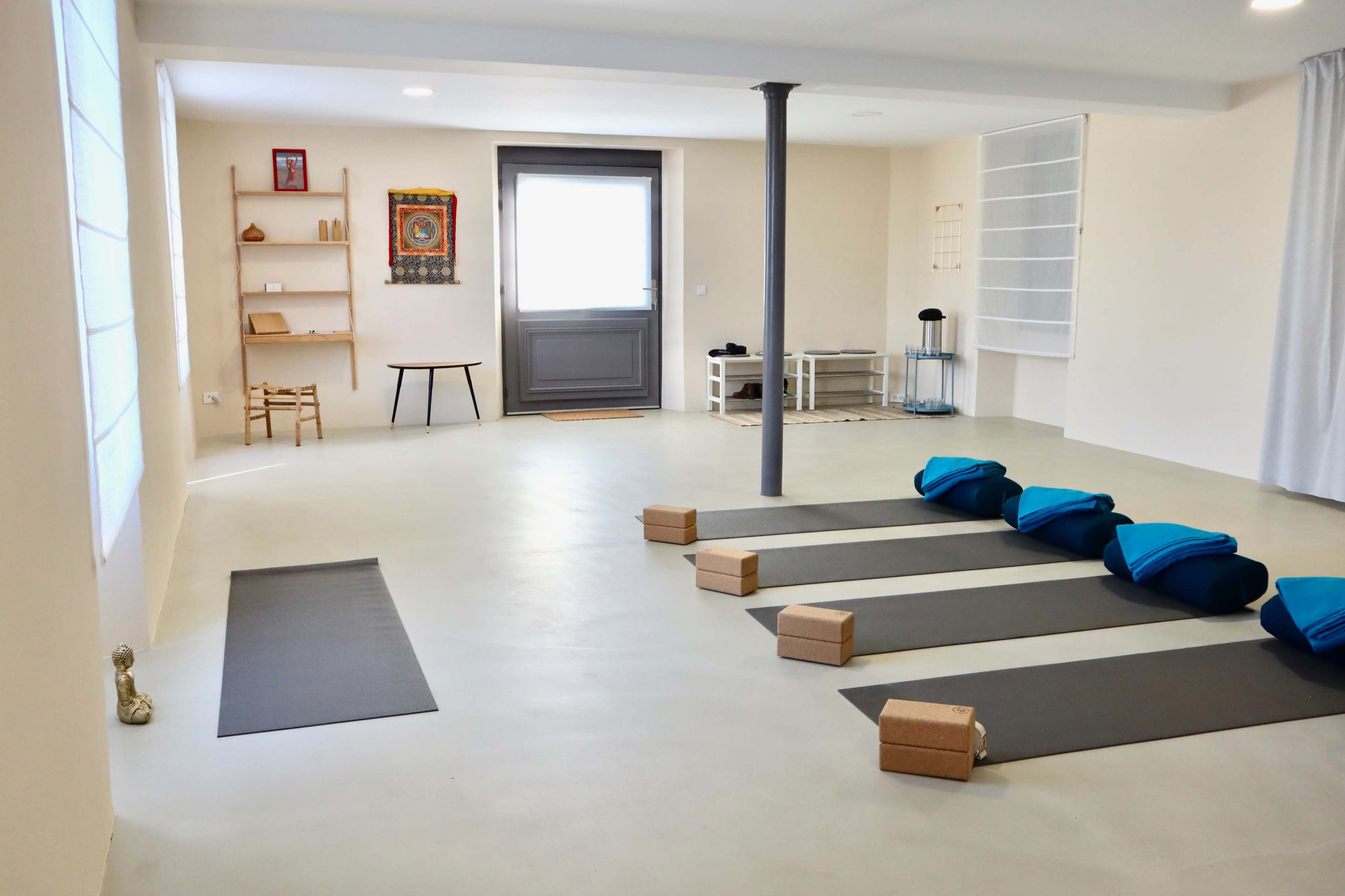 A spacious, minimalistic yoga studio featuring exercise mats, blocks, and a few pieces of furniture.