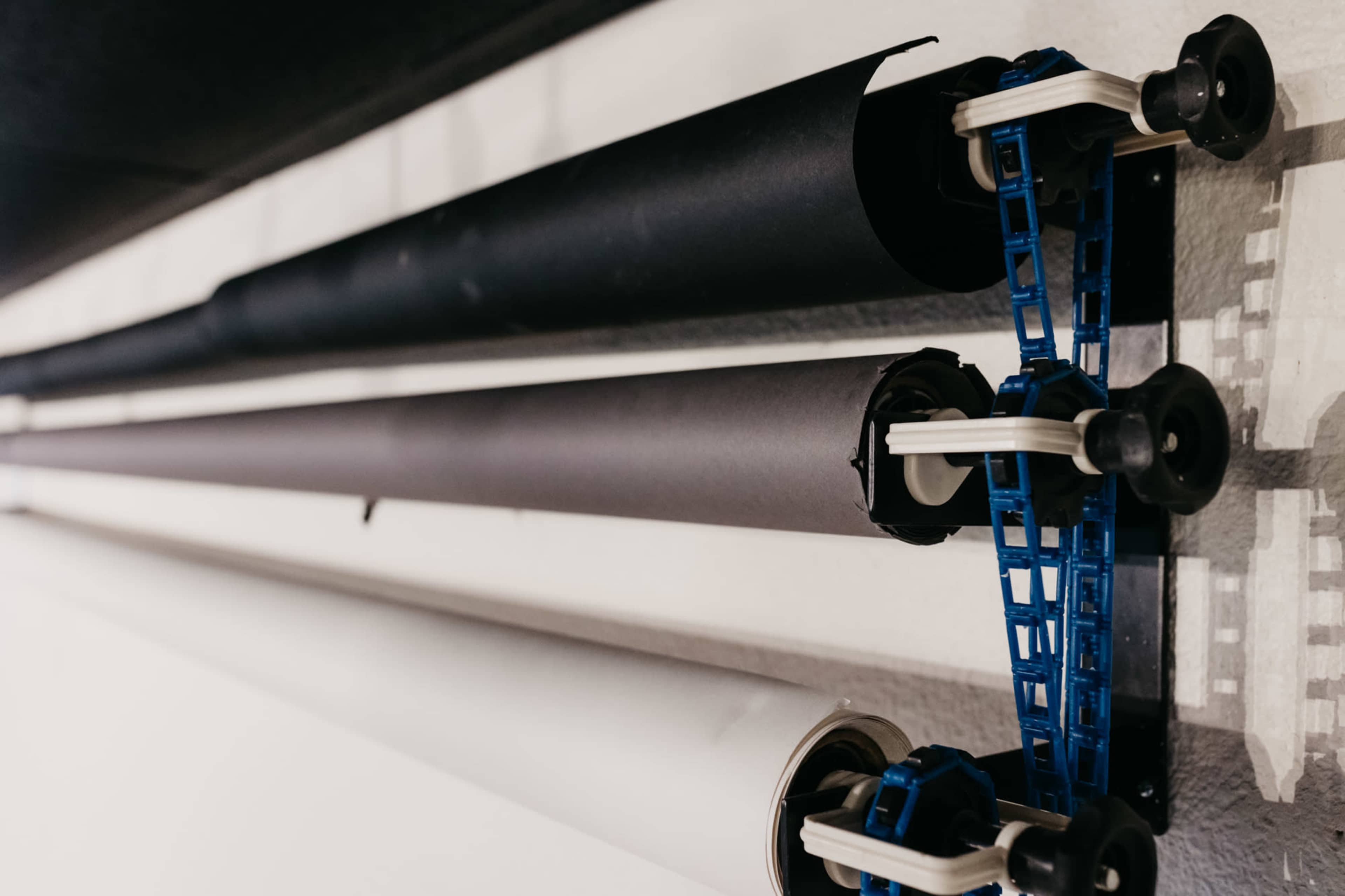A wall-mounted roll holder with three rolls of paper: two black and one white.