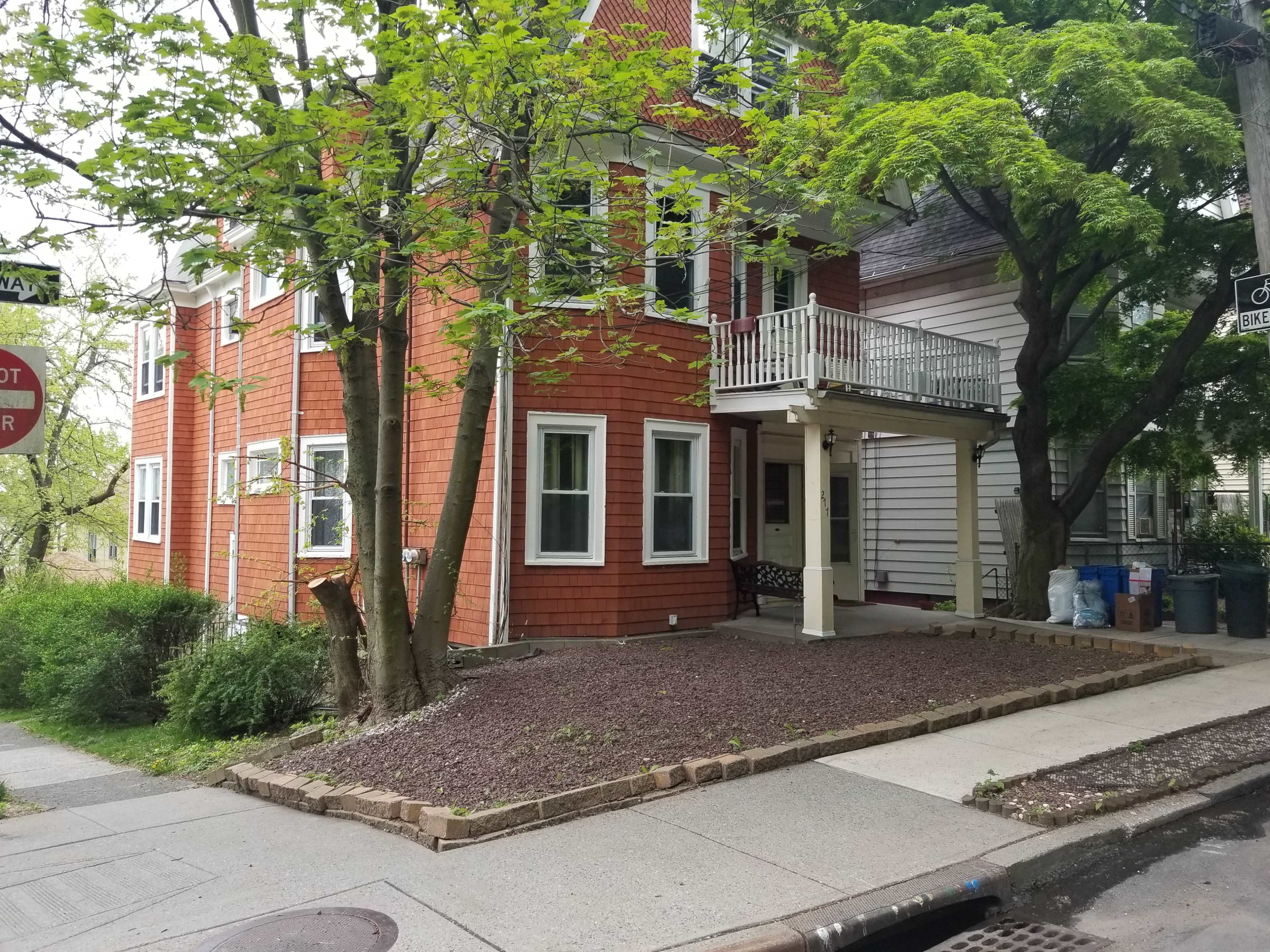 A two-story orange-shingled house with a covered porch and a small garden area next to a sidewalk.