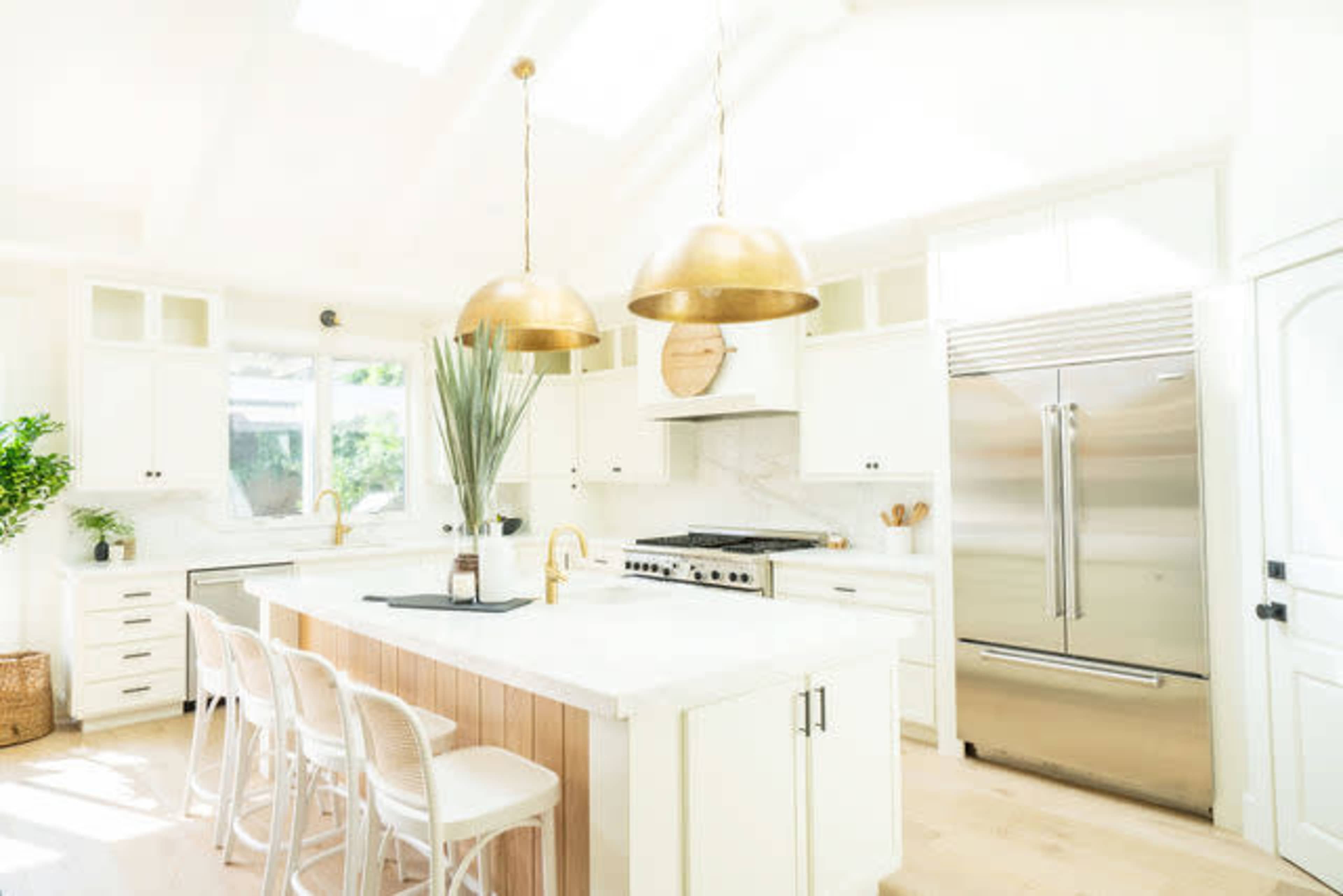 A bright, modern kitchen with white cabinetry, a large island featuring bar stools, and two gold pendant lights hanging overhead.