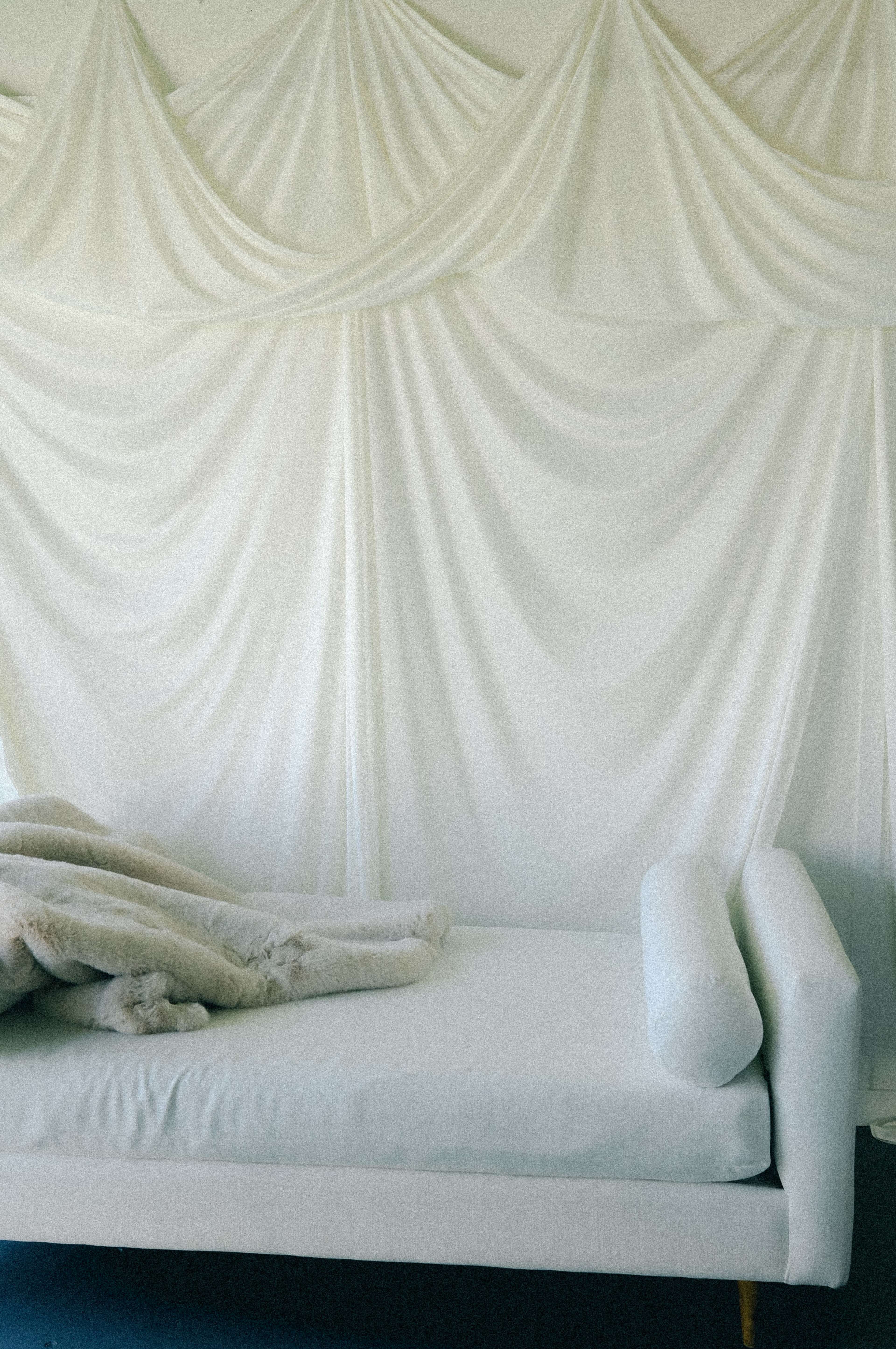 A white daybed is positioned against a draped white fabric wall.