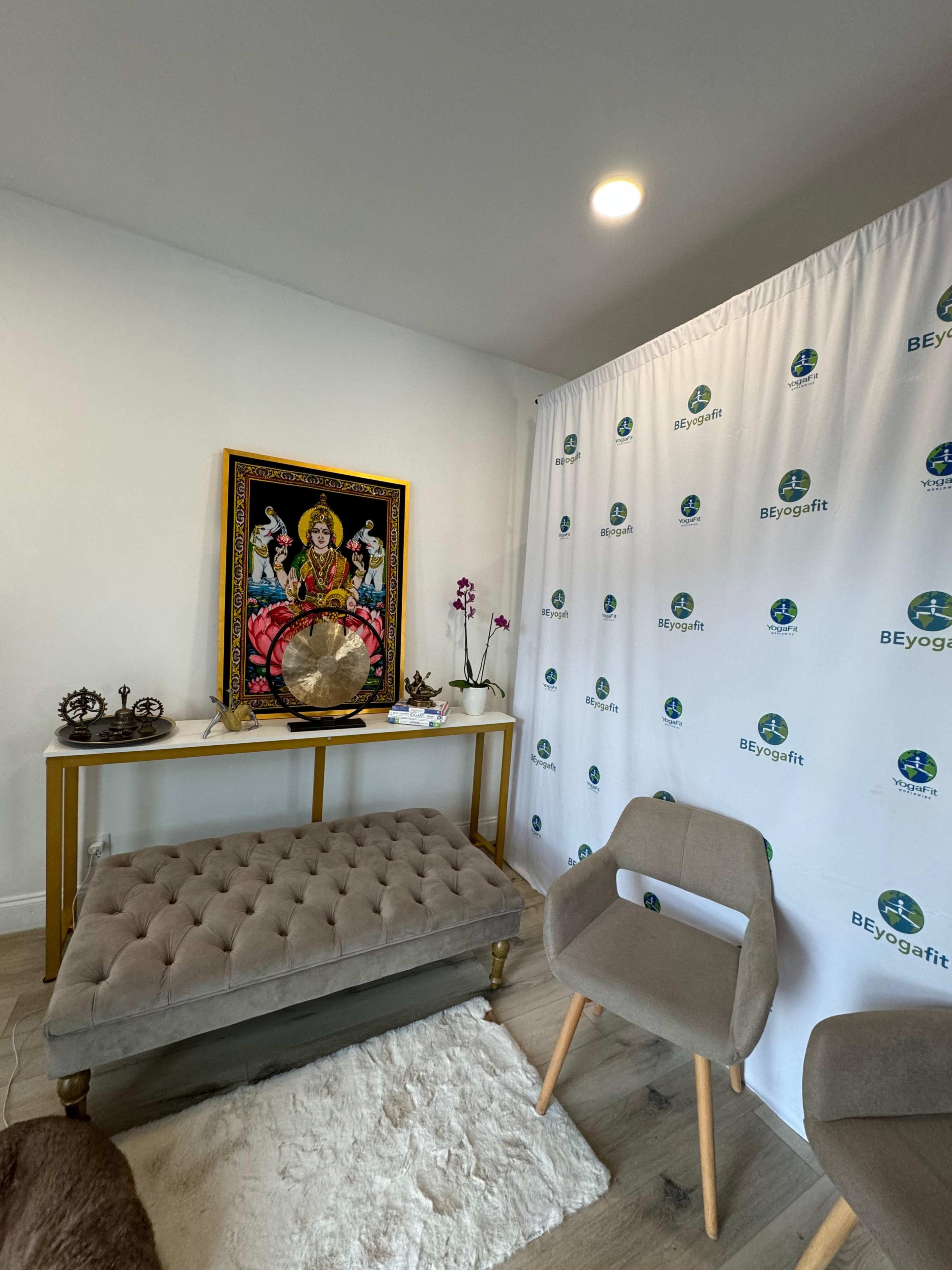 A yoga studio corner with a decorative altar featuring a colorful painting, a globe, and a tufted bench, adjacent to a wall draped with a branded banner.