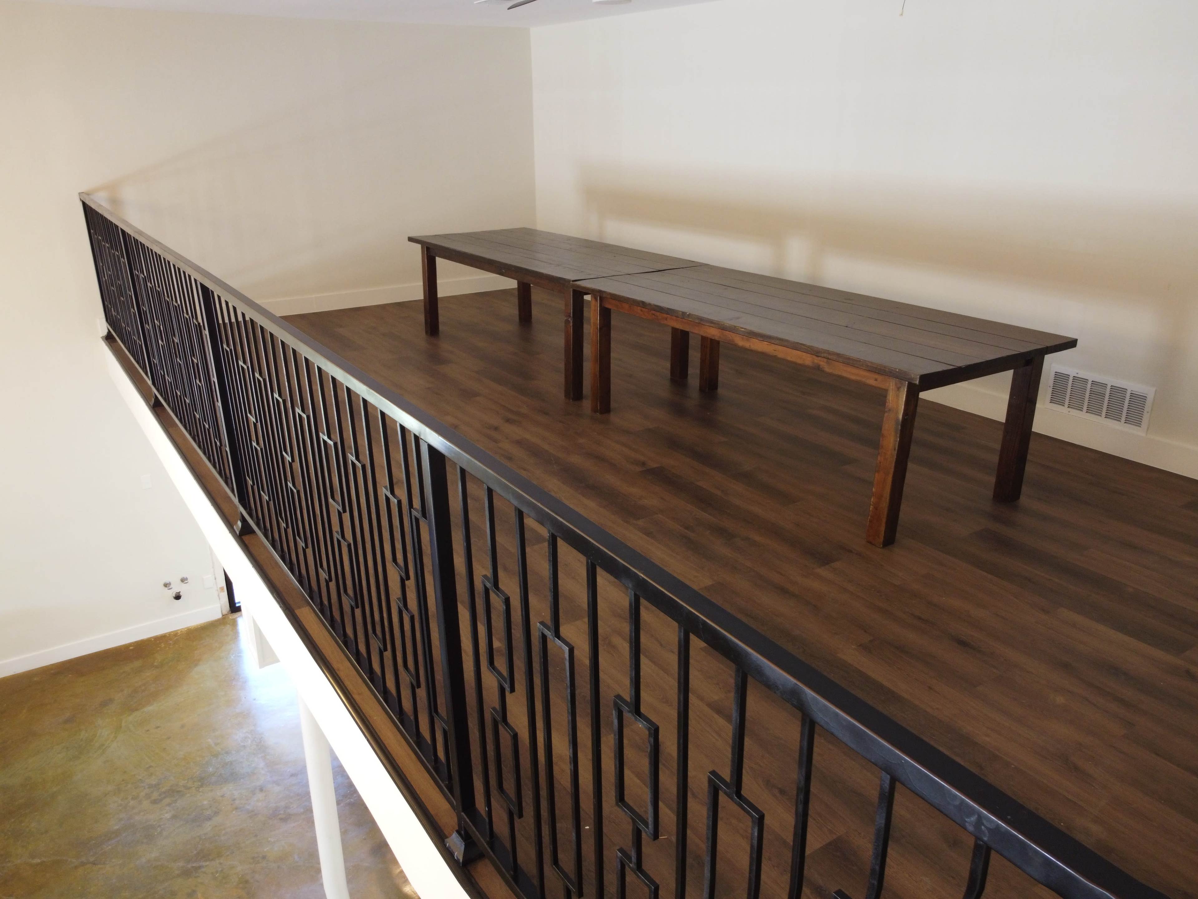 A second-floor space features two wooden tables placed on a polished floor, bordered by a decorative black railing.