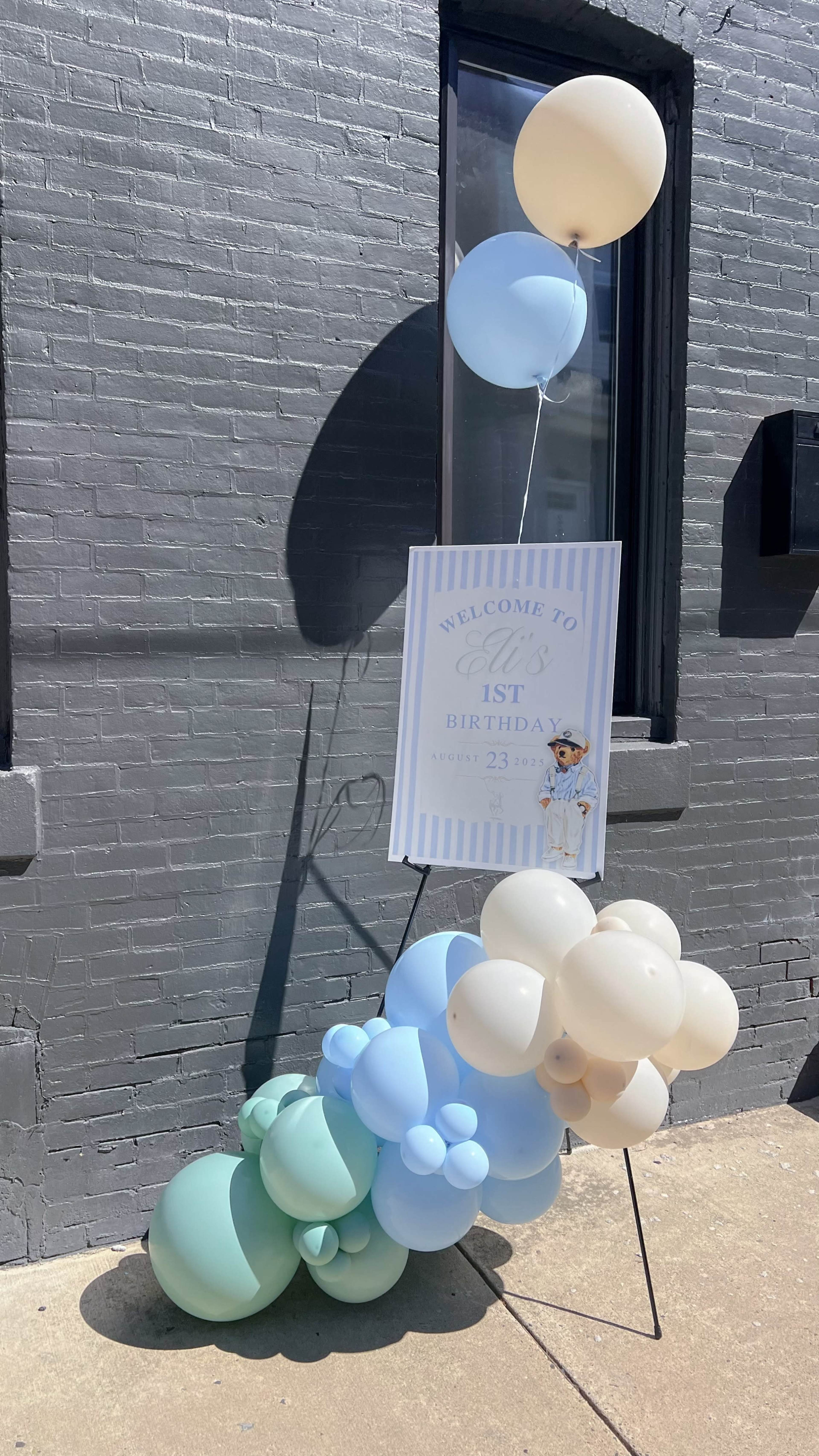 A decorative display for a first birthday celebration features a sign surrounded by pastel balloons in shades of blue and cream.