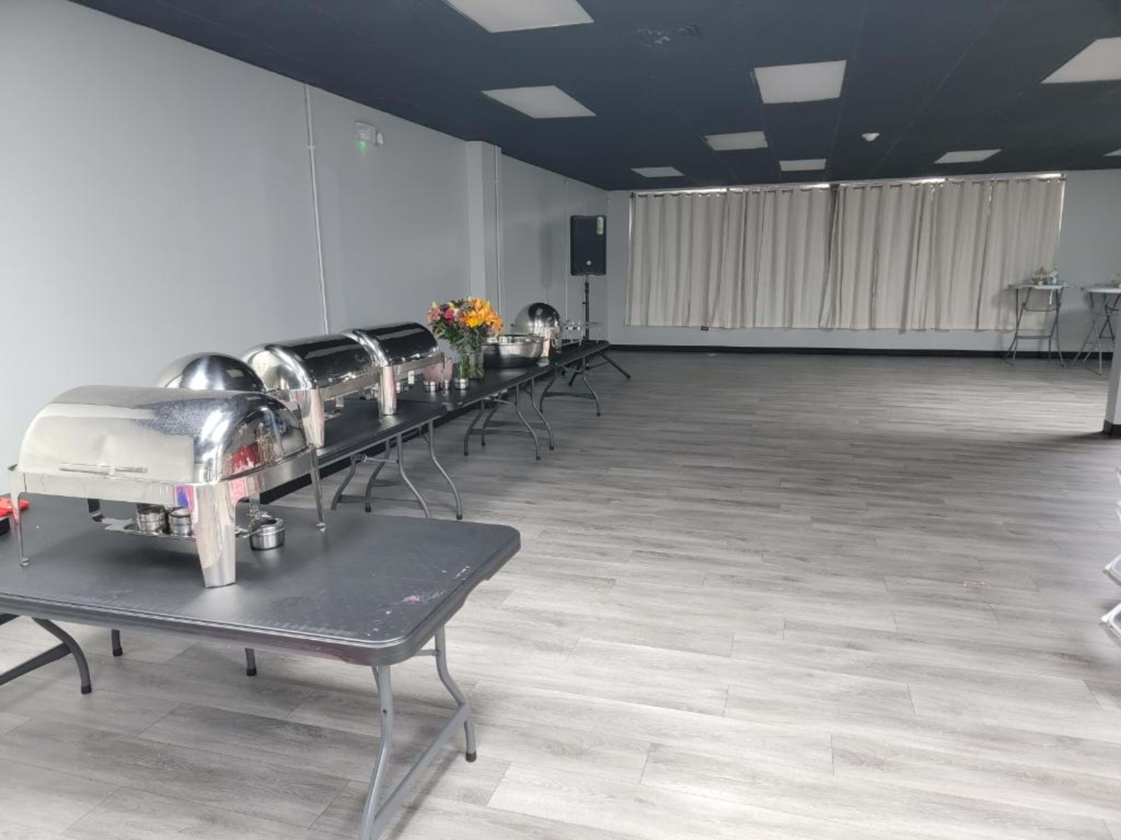 A spacious room with several chafing dishes set on long tables, arranged neatly and surrounded by a lightly decorated space.