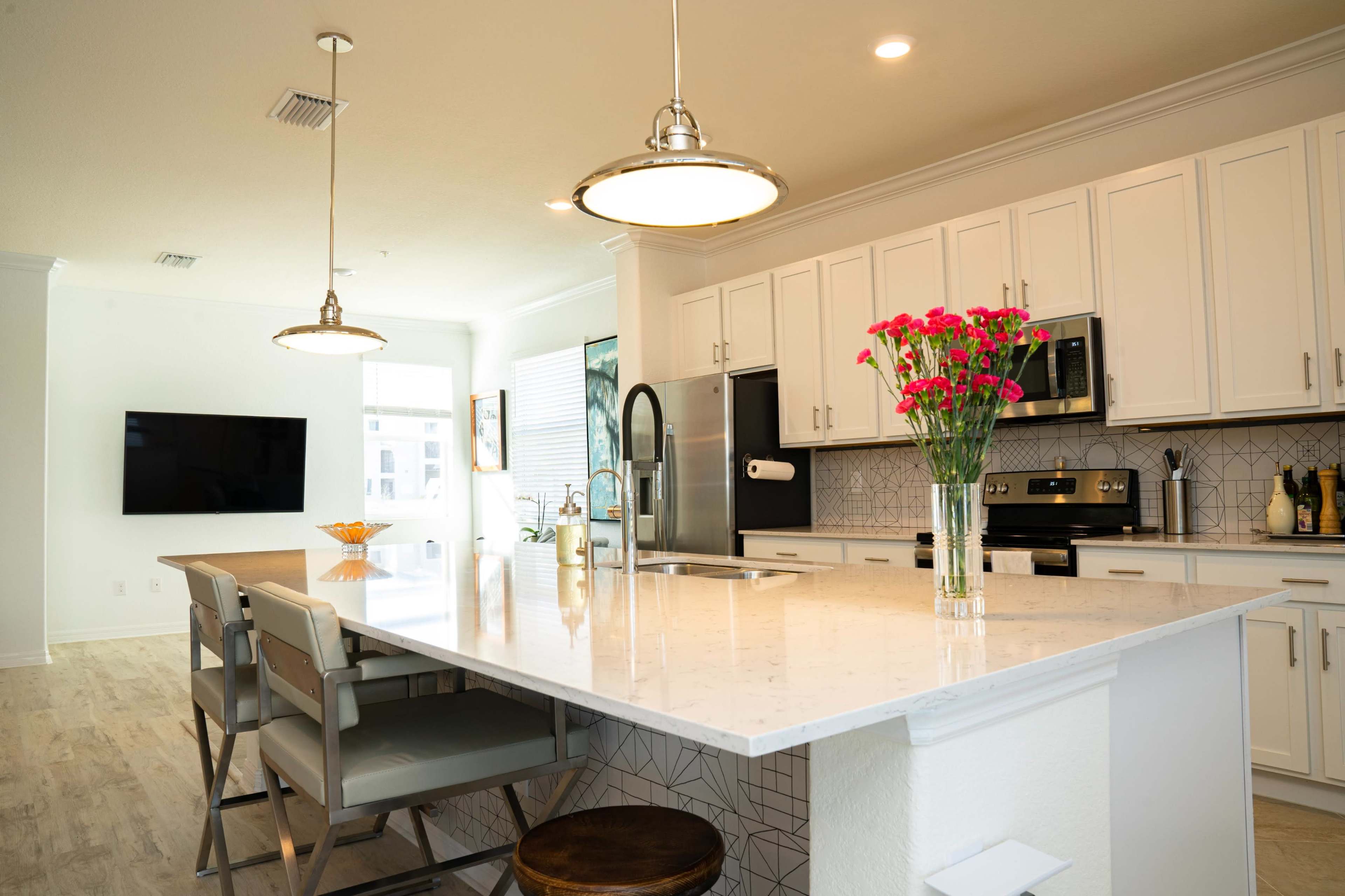 A modern kitchen features white cabinetry, stainless steel appliances, a large island with seating, and a vase of pink flowers on the countertop.