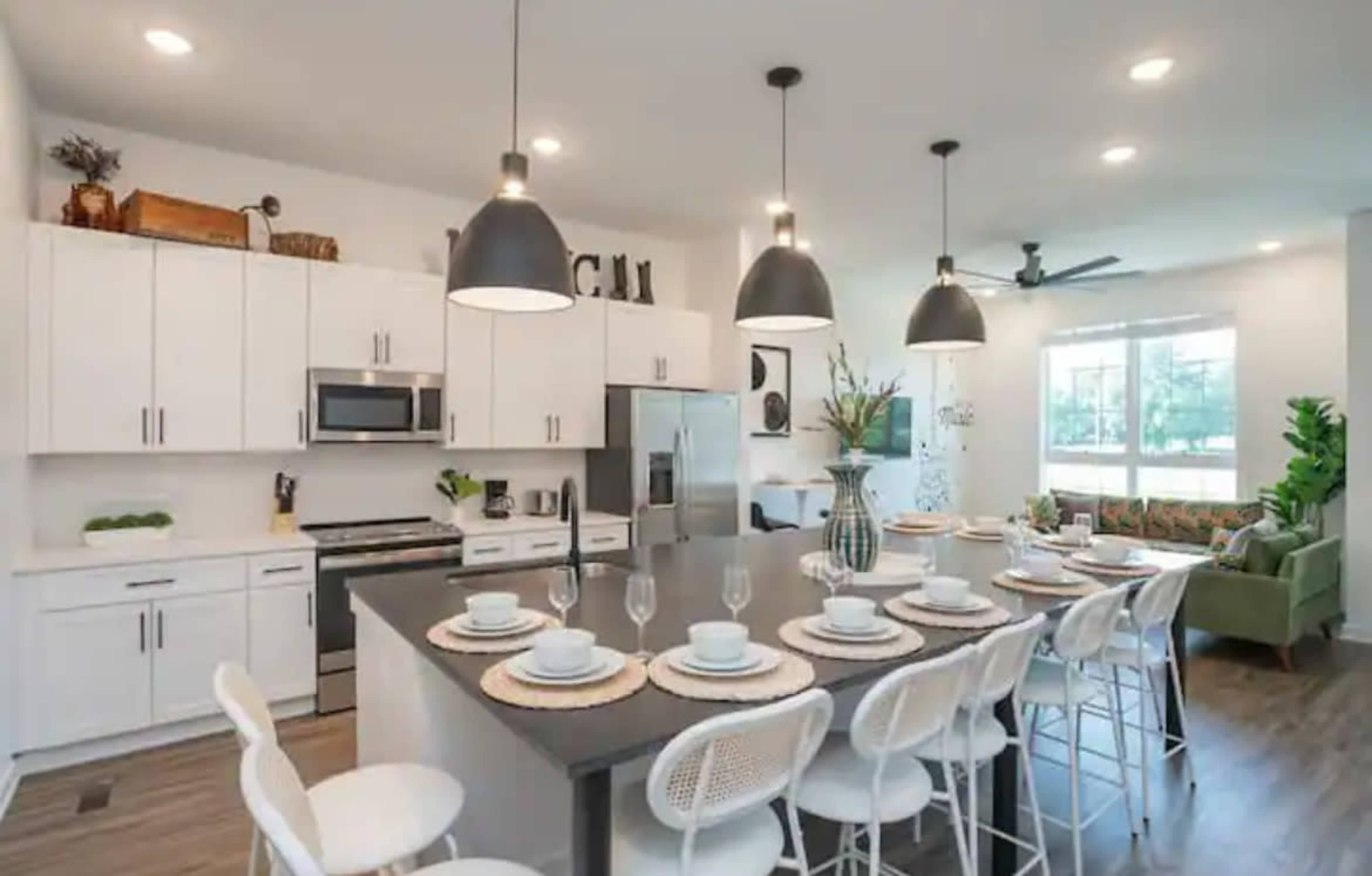 A modern kitchen features white cabinetry, stainless steel appliances, and a large island with bar seating for eight.