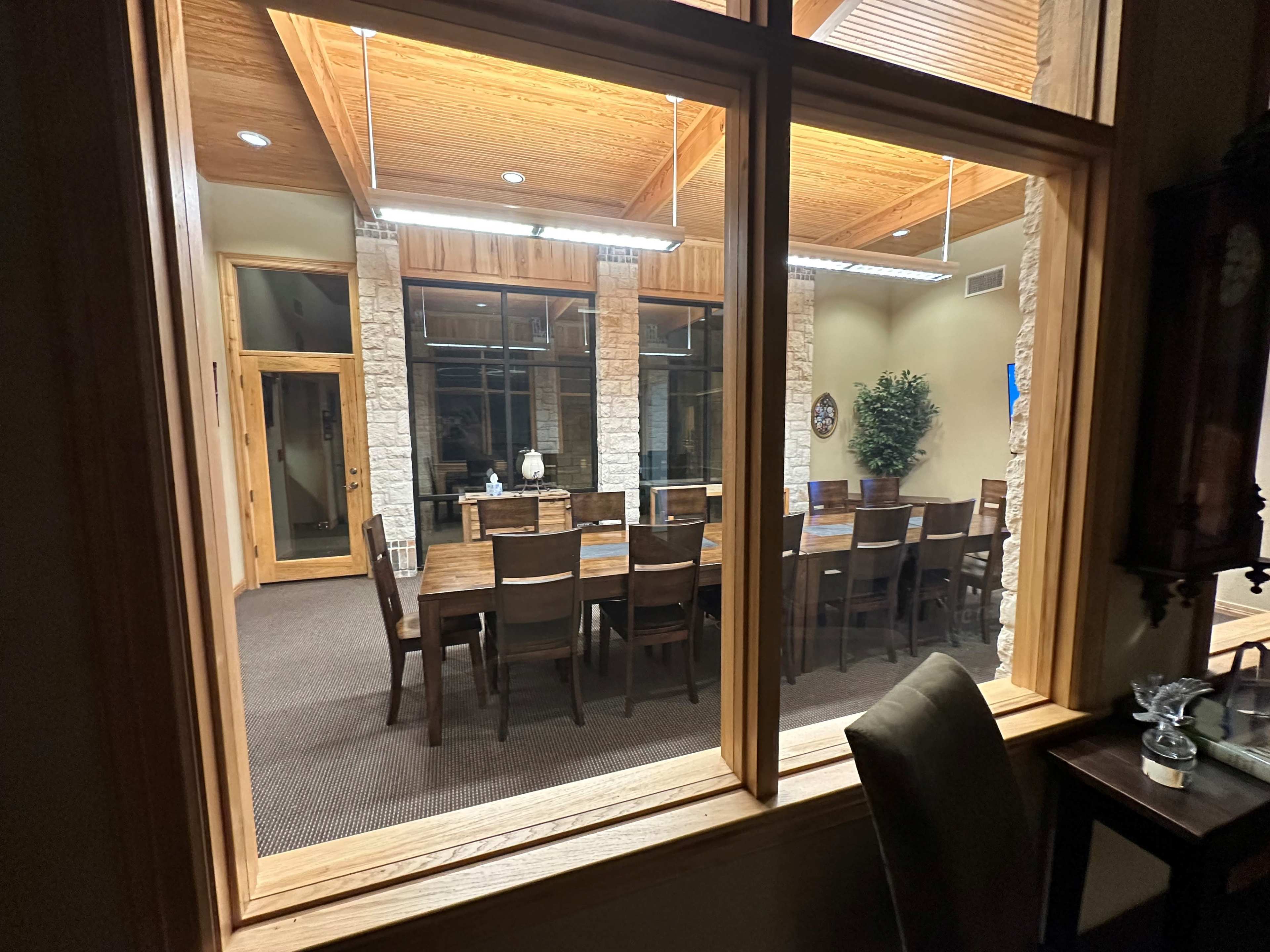 A spacious dining room with a long wooden table and chairs is viewed through a large window.