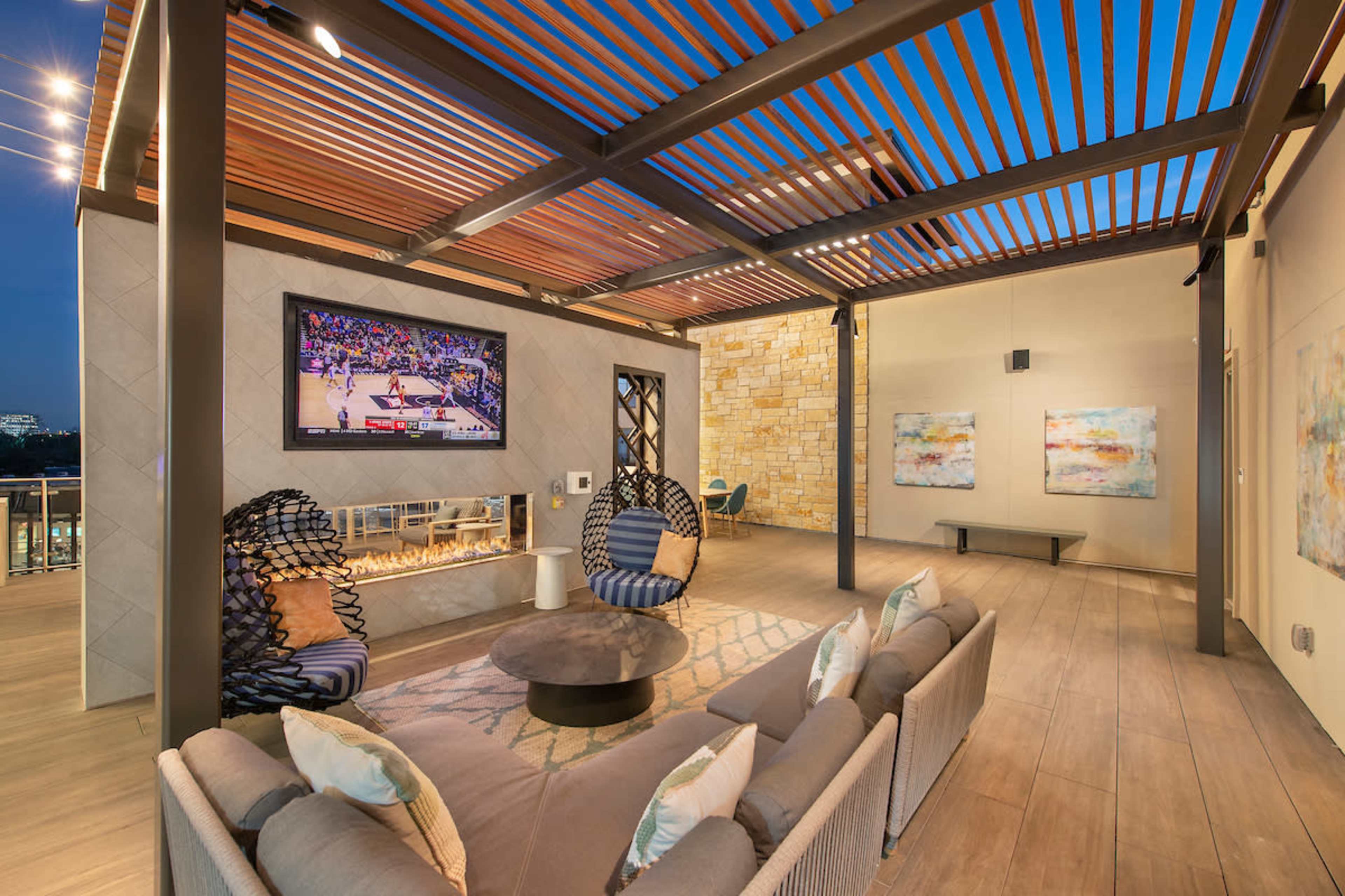 A modern outdoor living space features a television mounted on the wall, a cozy seating area with a circular coffee table, and decorative wall art.