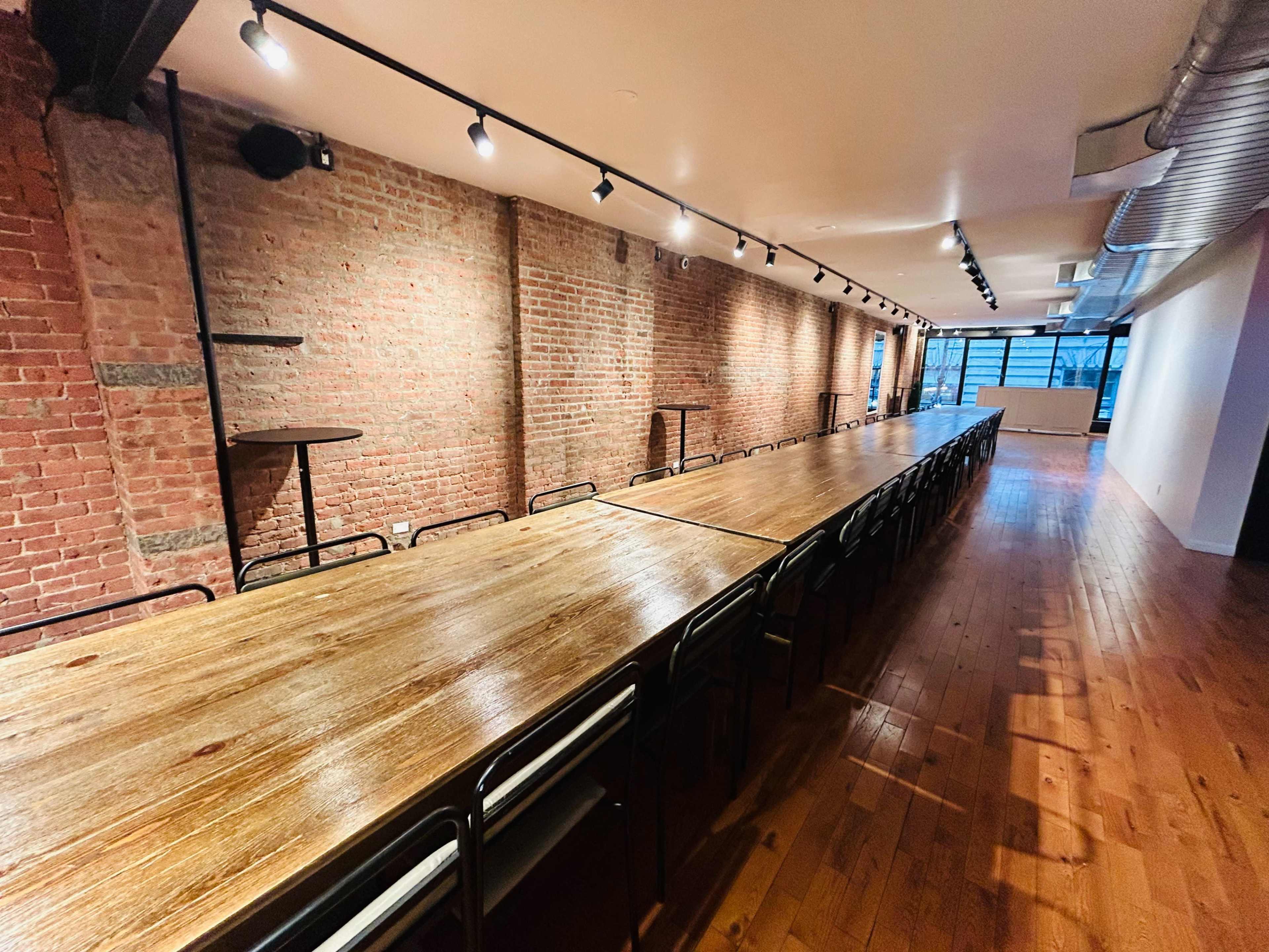 The image shows a long, wooden table in a spacious room with exposed brick walls and industrial lighting.