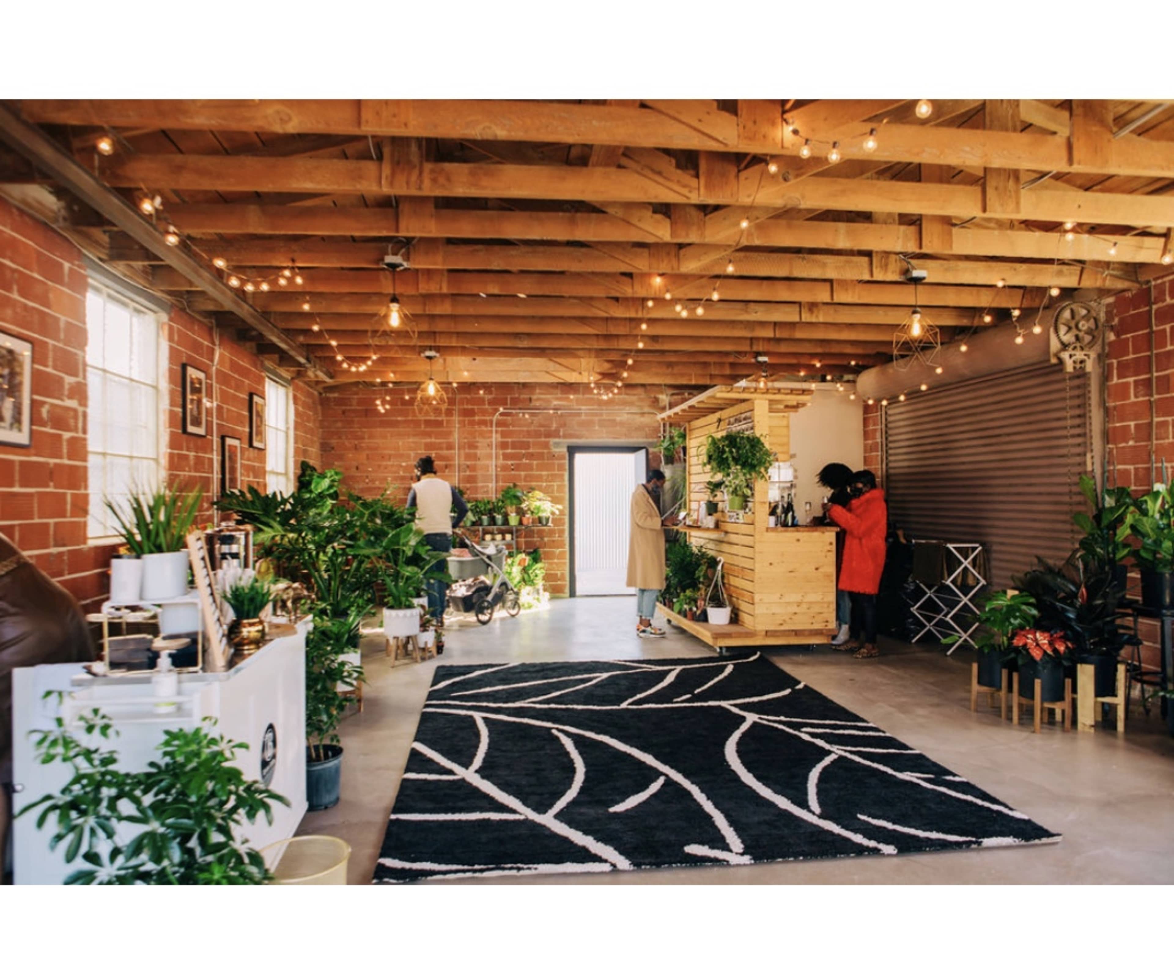 The spacious interior features a rustic wooden ceiling, potted plants, and a central counter with two people engaged in conversation.