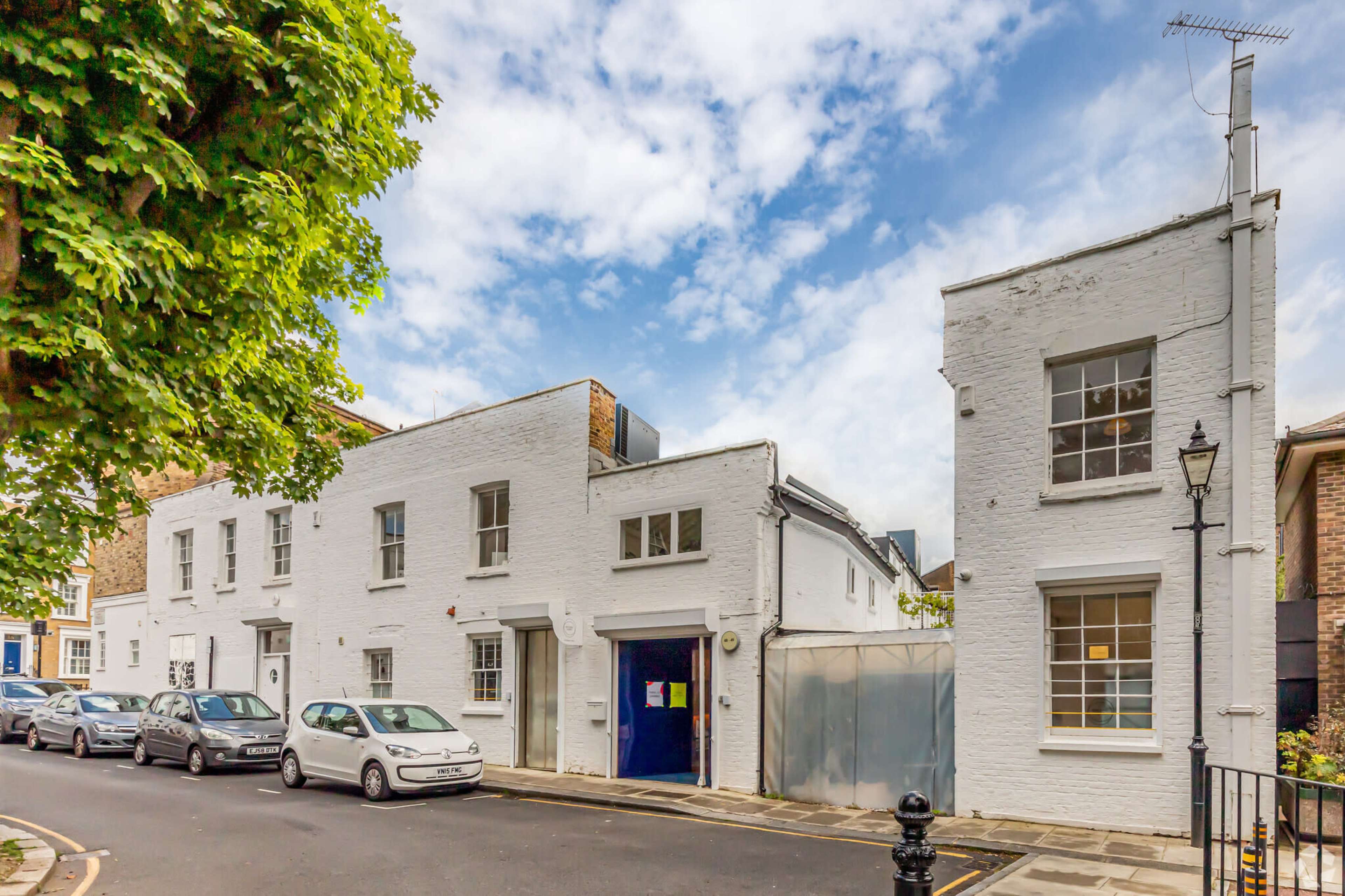 The image shows a white, two-story building on a street corner, with several parked cars and a cloudy sky above.