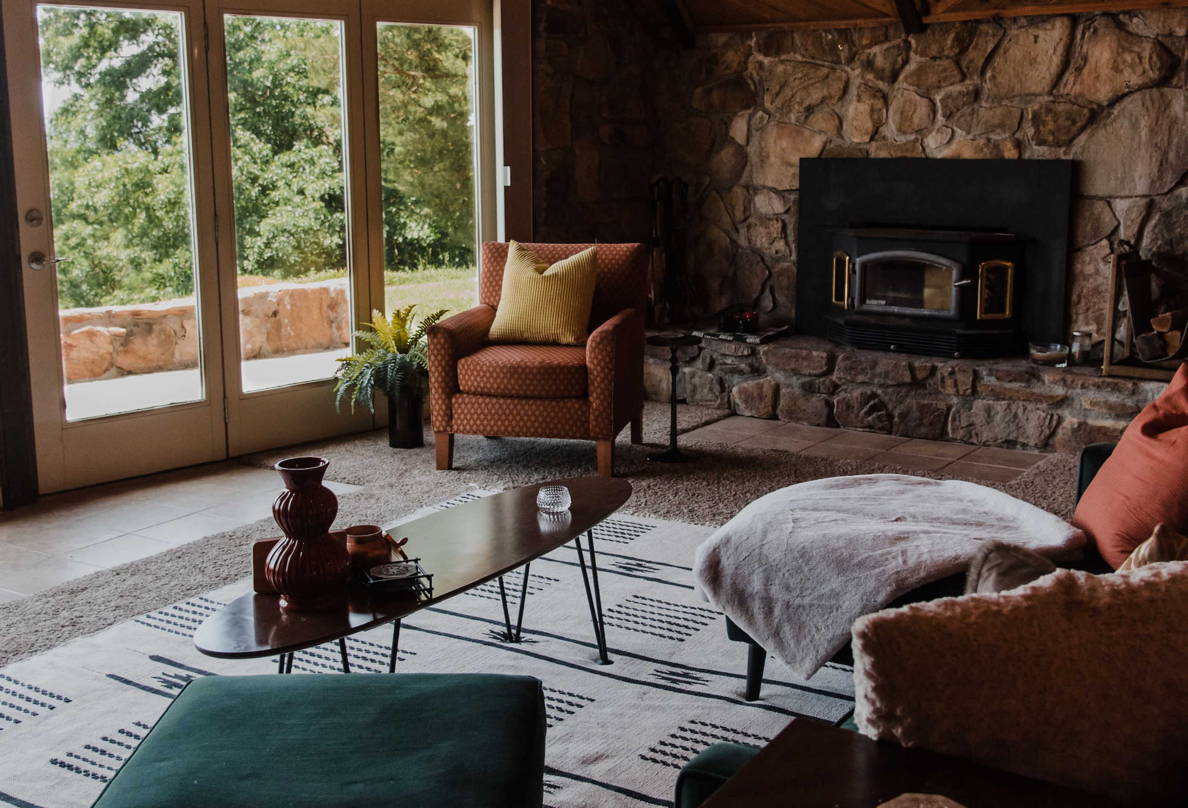 The living room features a stone fireplace, large glass doors leading to an outdoor area, and a combination of patterned rugs and furniture.