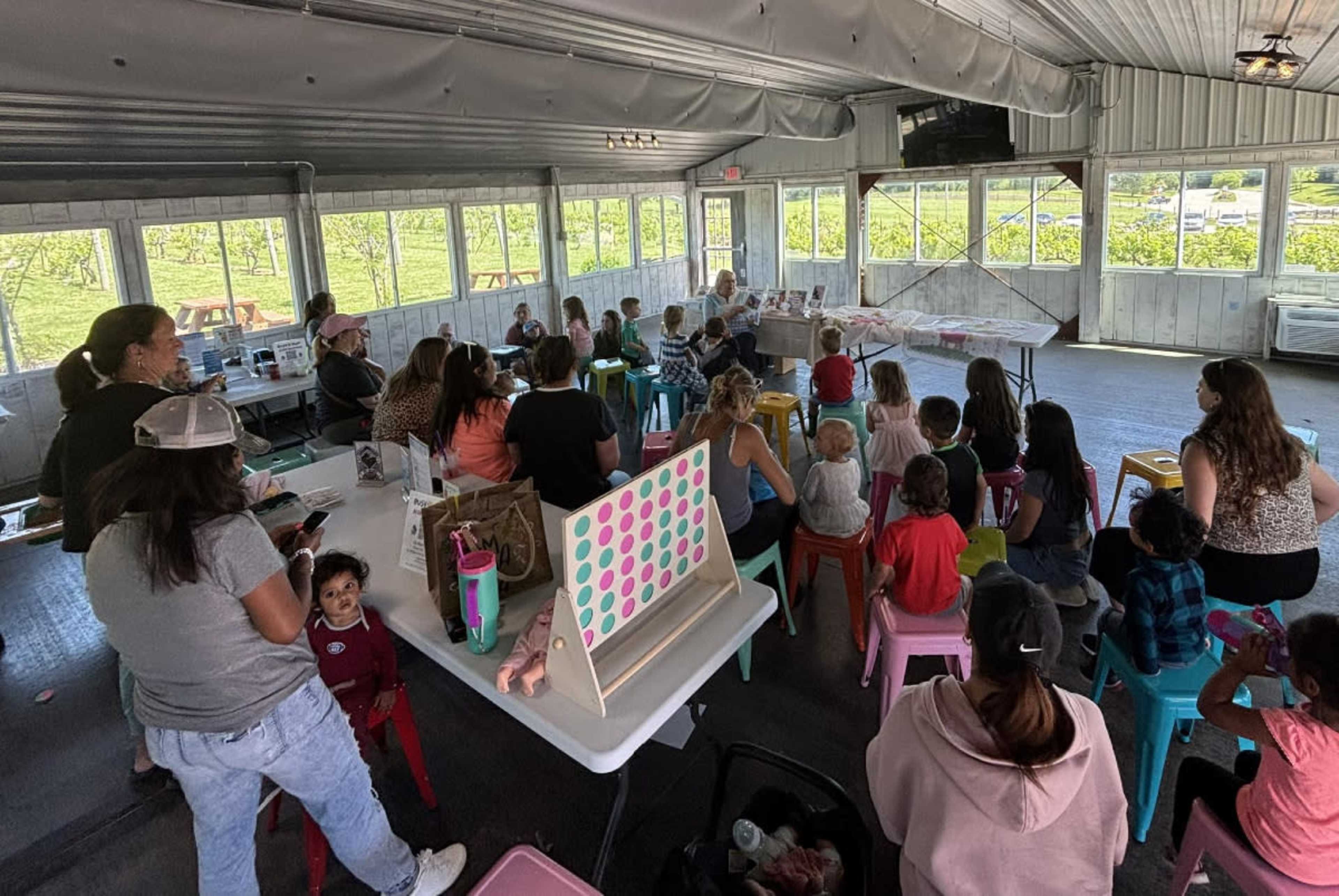 A group of children and adults are seated in a well-lit indoor space, watching a presentation or activity.