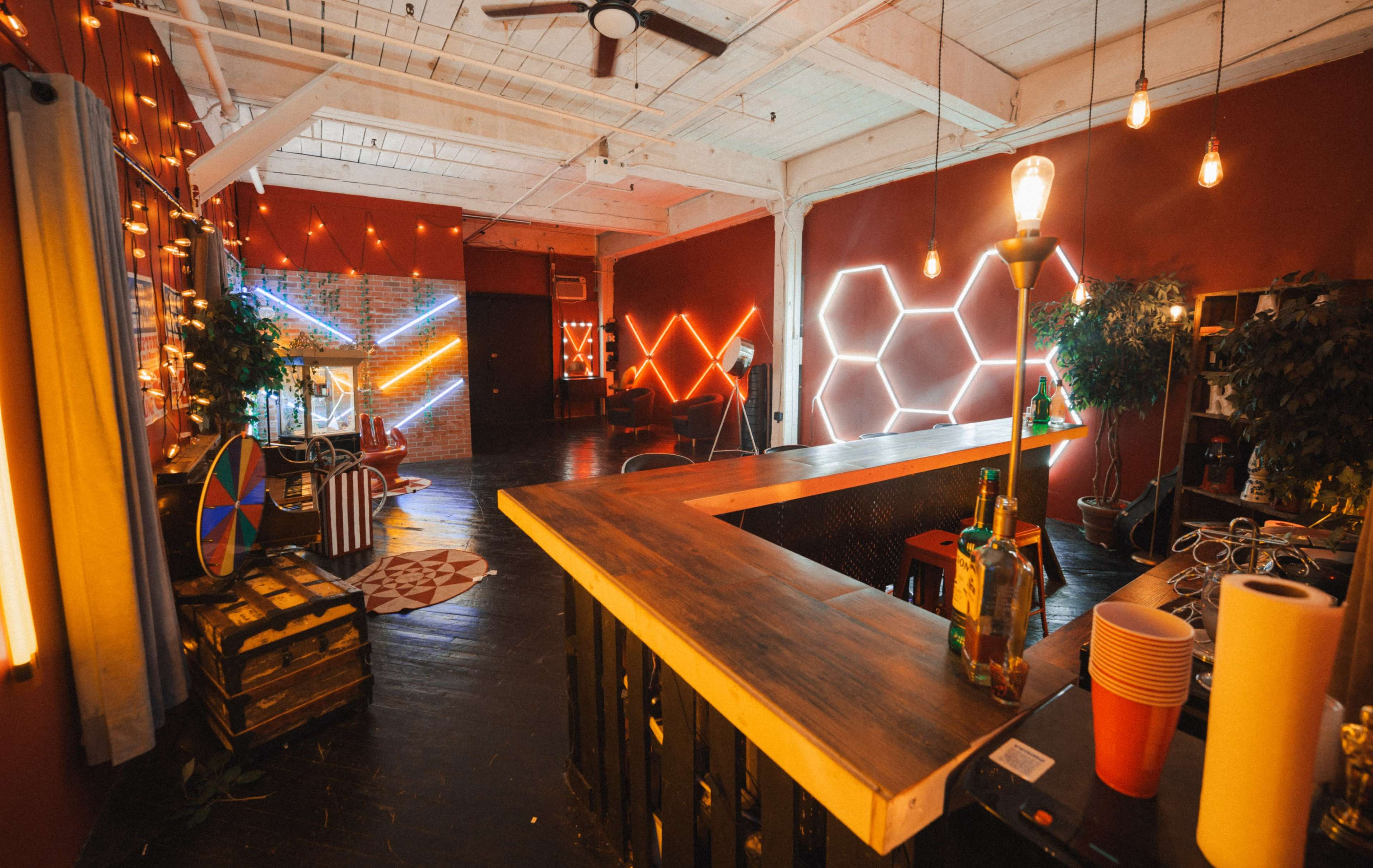 The image shows a modern interior space with a wooden bar, vibrant neon lights on the walls, and various decorative elements, creating a lively atmosphere.