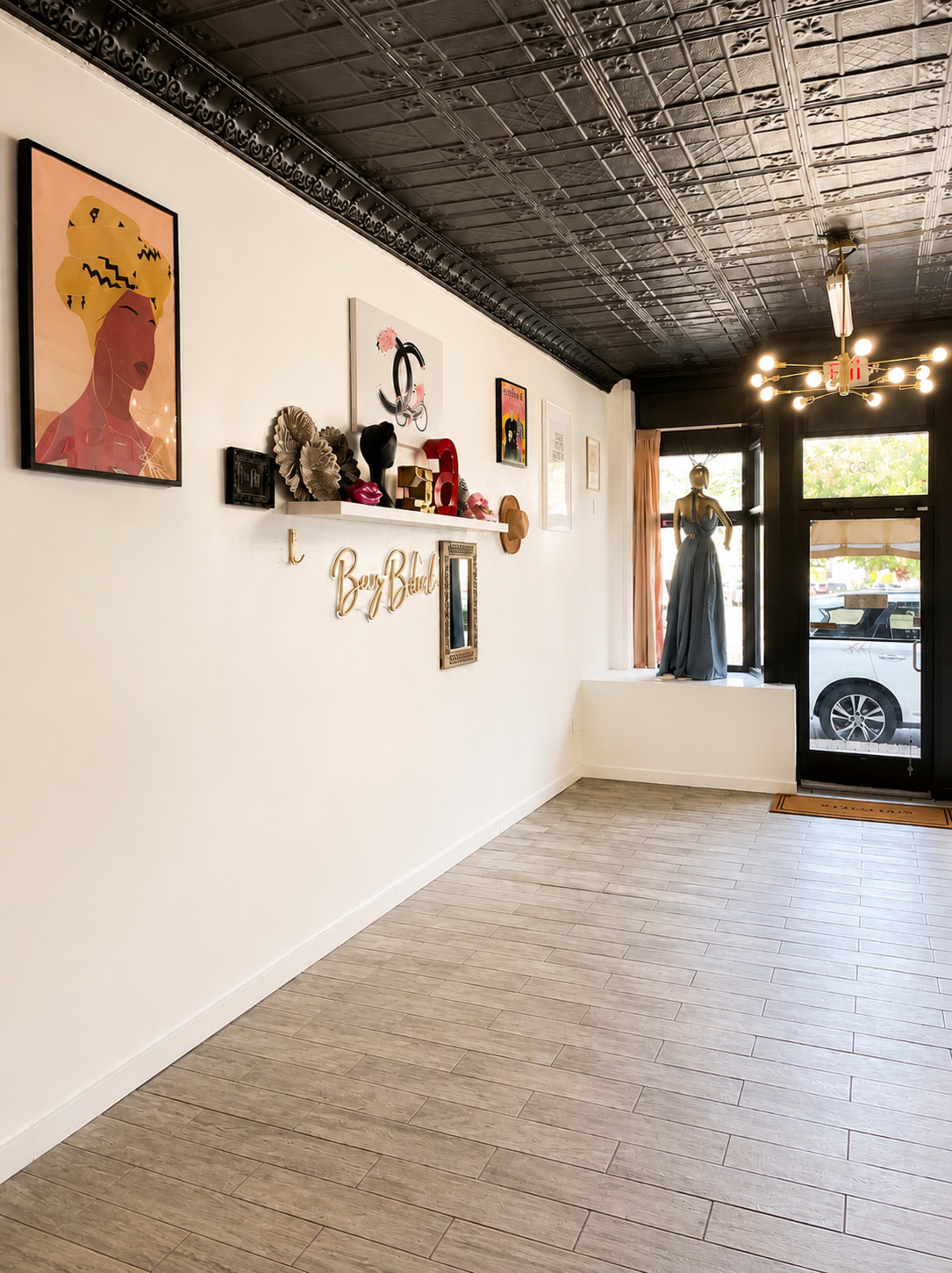 The image shows a stylish interior of a shop with various artworks displayed on the walls and a mannequin dressed in a long gown positioned near the entrance.